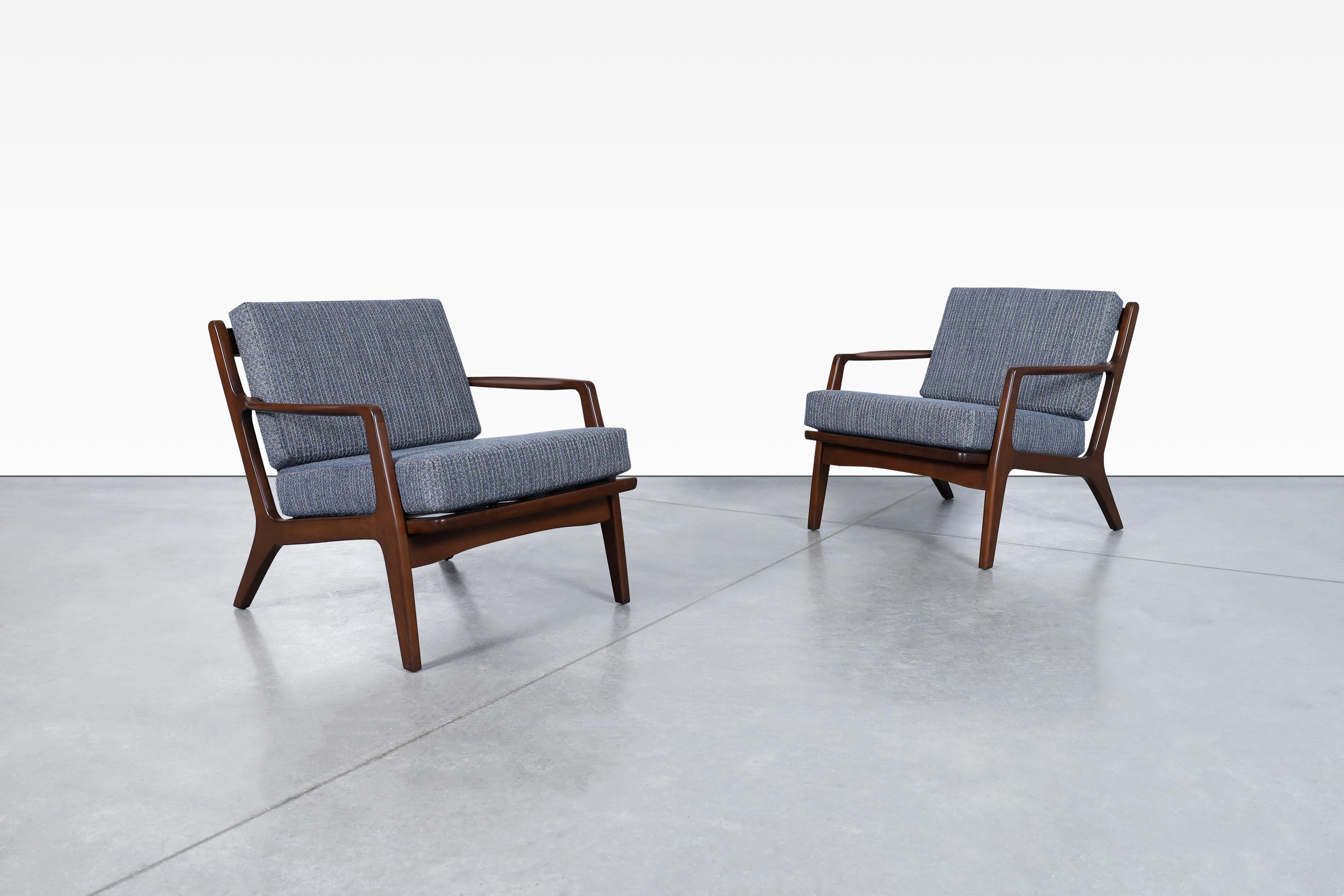 Stunning Danish modern walnut lounge chairs designed by the iconic Danish designer Ib Kofod-Larsen for Selig in Denmark, circa 1960s. These chairs are truly stunning! The solid walnut frame is expertly crafted to create a sleek and elegant profile