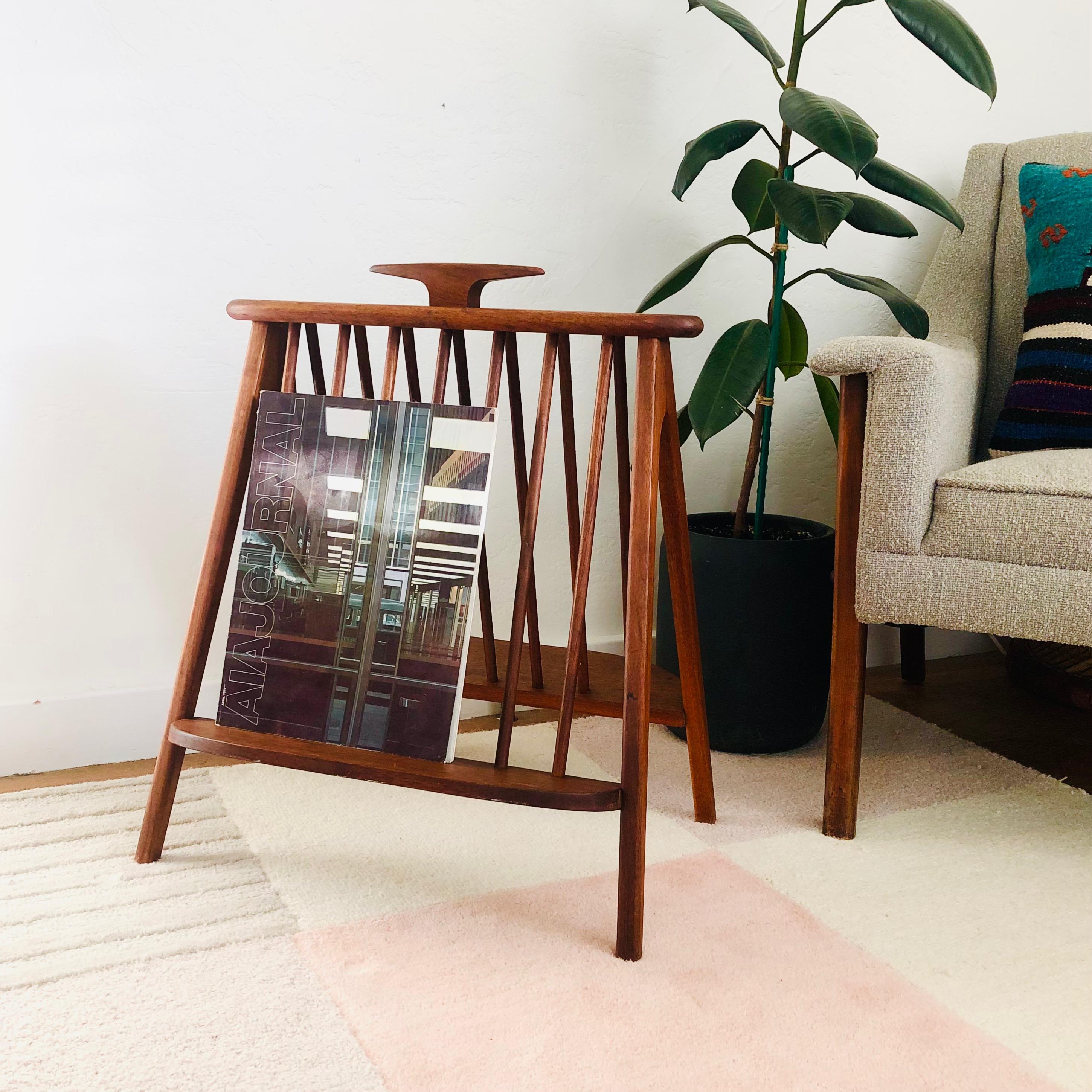 A mid-century walnut magazine rack designed by Arthur Umanoff for Washington Woodcraft. Elegantly designed with a spindle back frame and 2 ledges for holding magazines or books on either sides. Topped off by a sculpted wood handle.
 