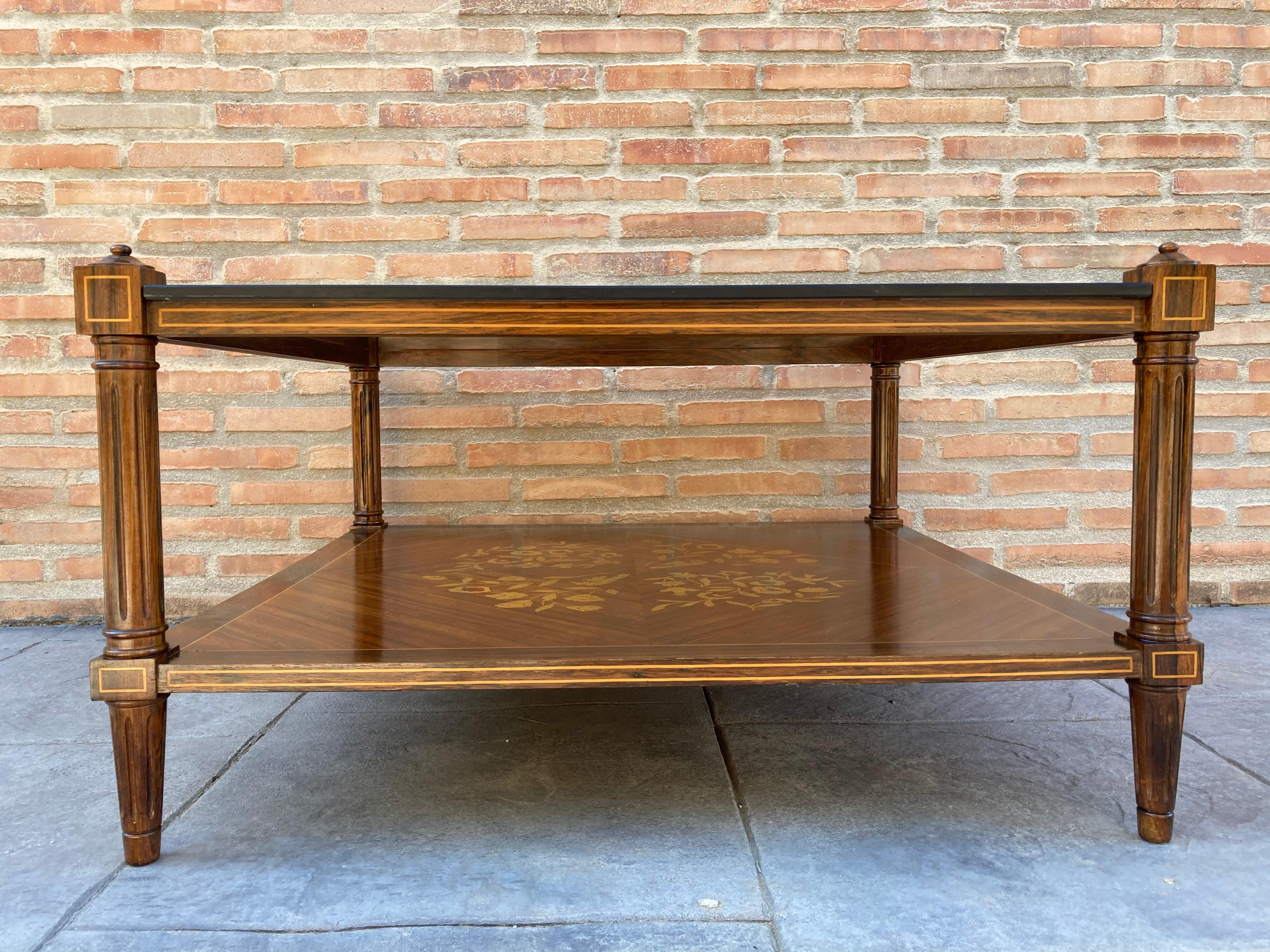 Mid-Century Modern two-tier side table or corner table with a square shape and four legs. 
The table has the entire base decorated with marquetry and the top is made in glass, is in excellent vintage condition, with age appropriate use.