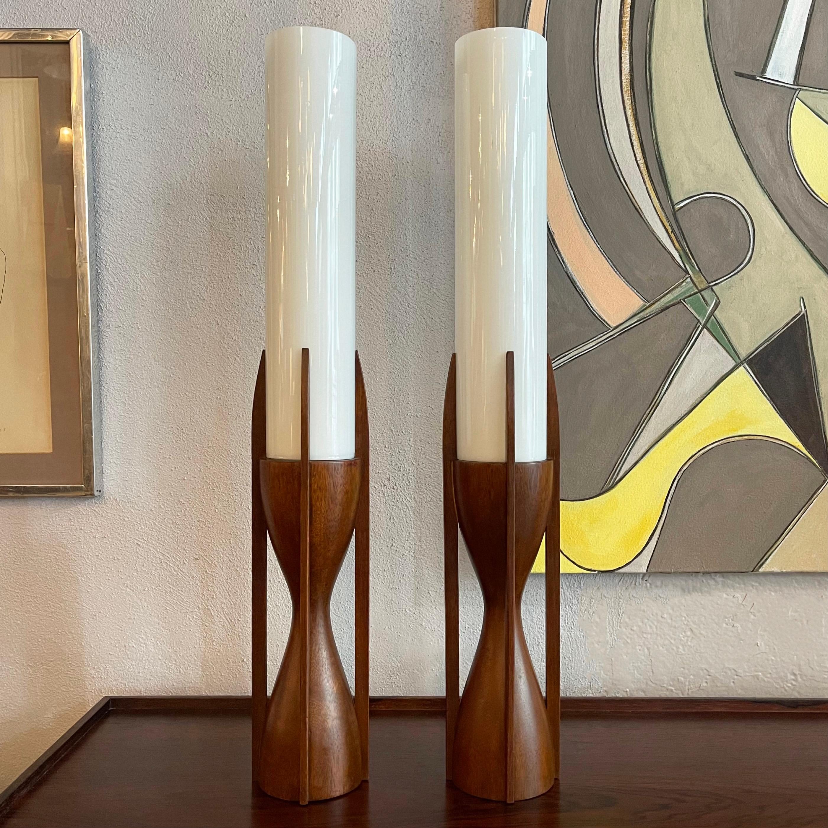 Impressive pair of mid-century modern, architectural table lamps by Byron Botker for Modeline Lamp Co. feature sculpted, hourlgass, walnut bases with 14 inch high milk glass cylinder shades fit into them. The lamps accept regular medium socket