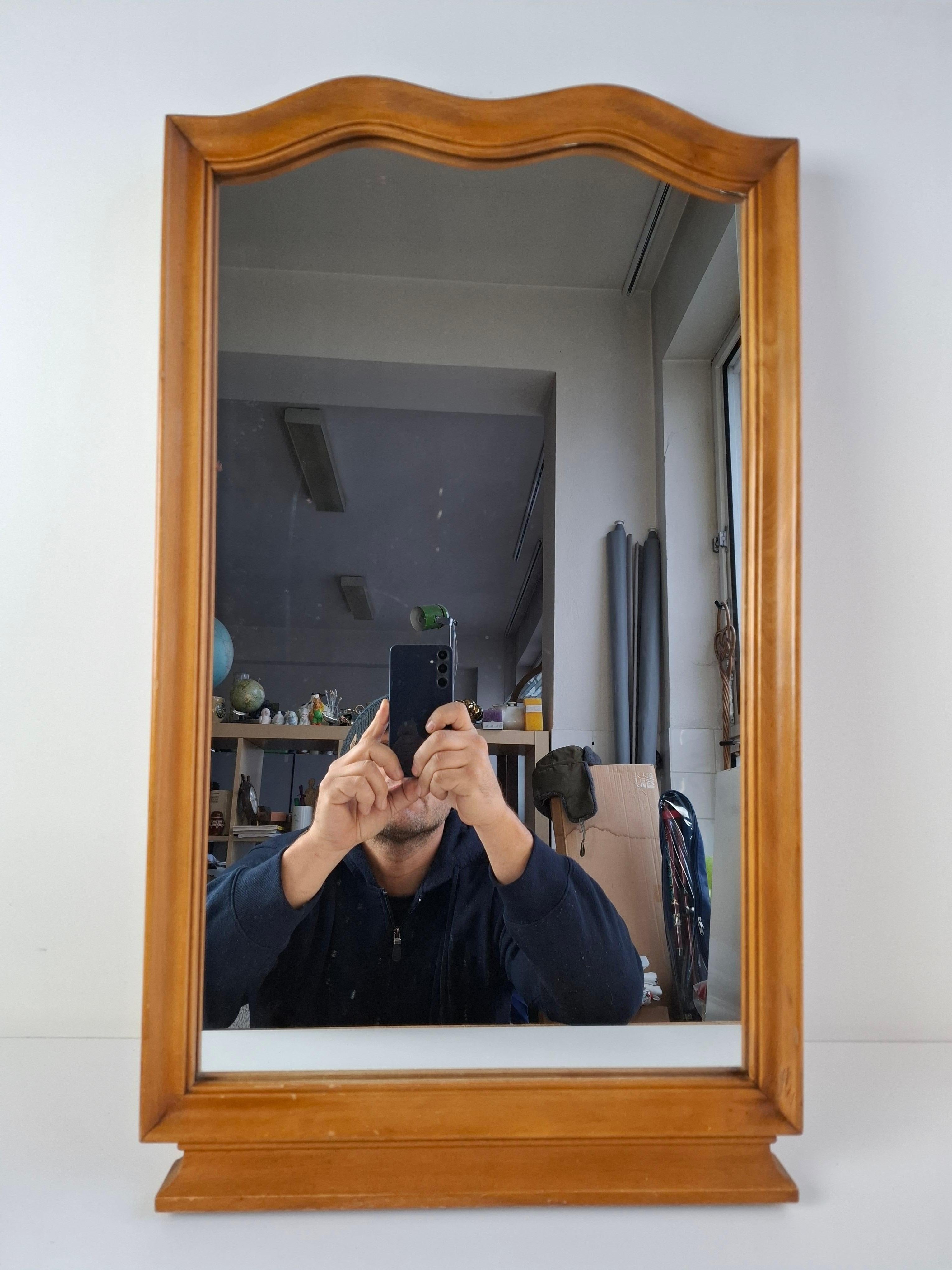 This mid-century mirror from 1960s Czechoslovakia features a sculpted walnut frame with gentle curves and a warm natural finish. The piece displays a tasteful aged patina that enhances its vintage authenticity. Its balanced proportions make it