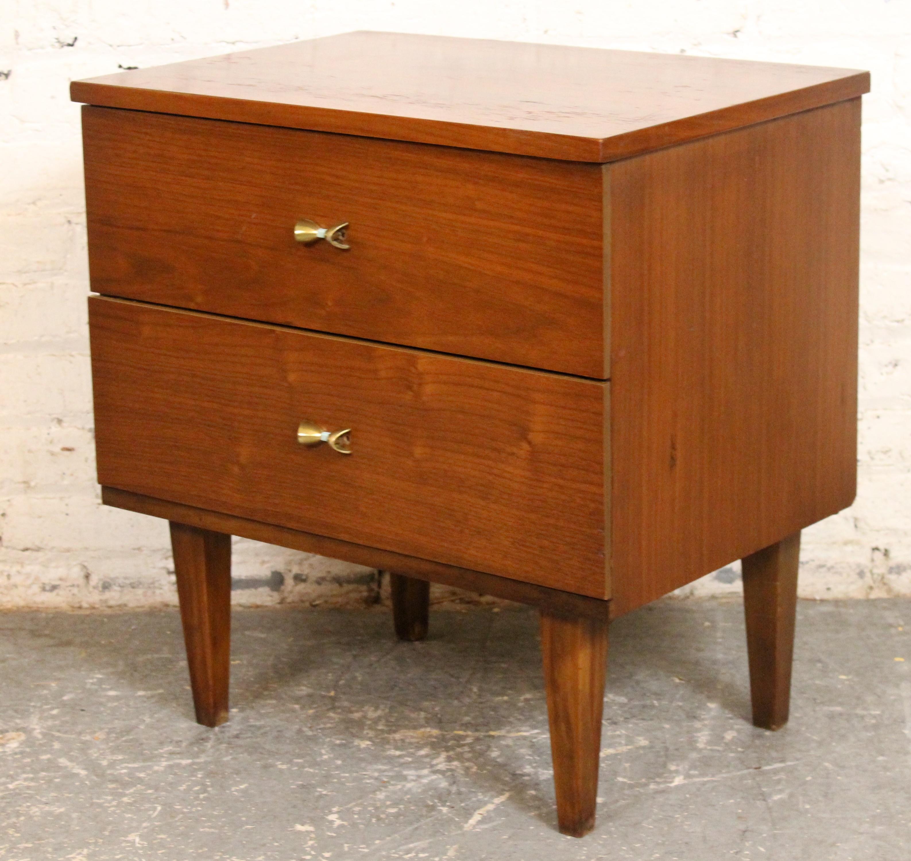 Elegante y funcional, esta mesilla de noche moderna de mediados de siglo está fabricada en madera de nogal, acentuada con tiradores de latón curvados. Sus líneas limpias y sus patas suavemente ahusadas reflejan la sencillez atemporal del diseño de