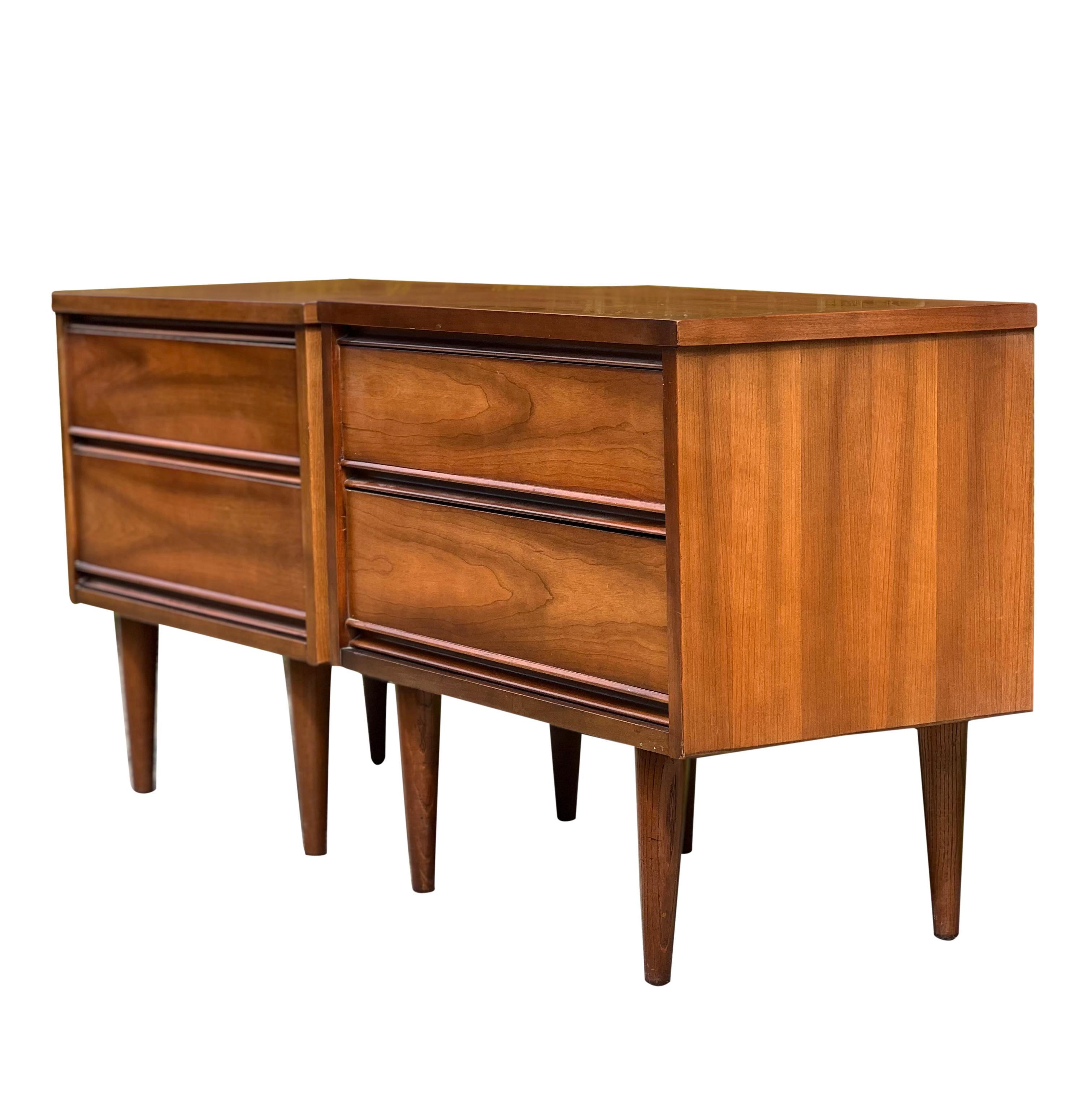 Lovely Mid Century walnut nightstands by Harmony House.

The stands feature a clean, classic Mid Century modern design with two dovetail drawers and tapered legs. The drawers have pulls carved along the bottom length of each one.

These are