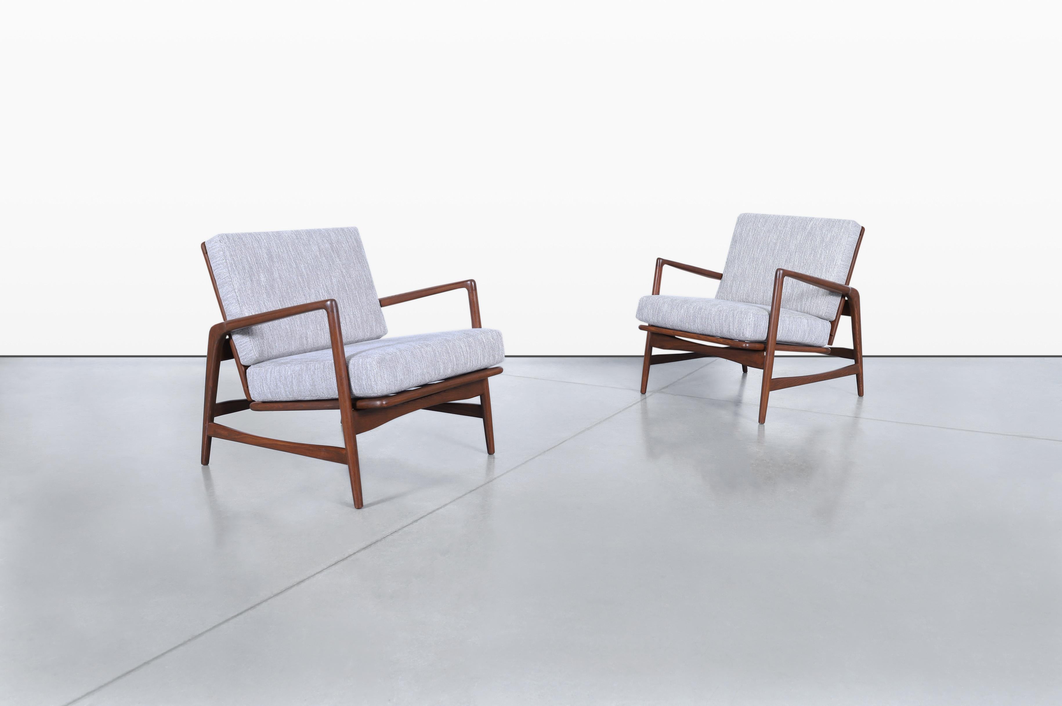 A stunning pair of mid-century modern reclining lounge chairs designed by the renowned Ib Kofod Larsen for Selig in the 1960s. These exquisite chairs feature solid walnut-stained oak frames that showcase the meticulous attention to detail