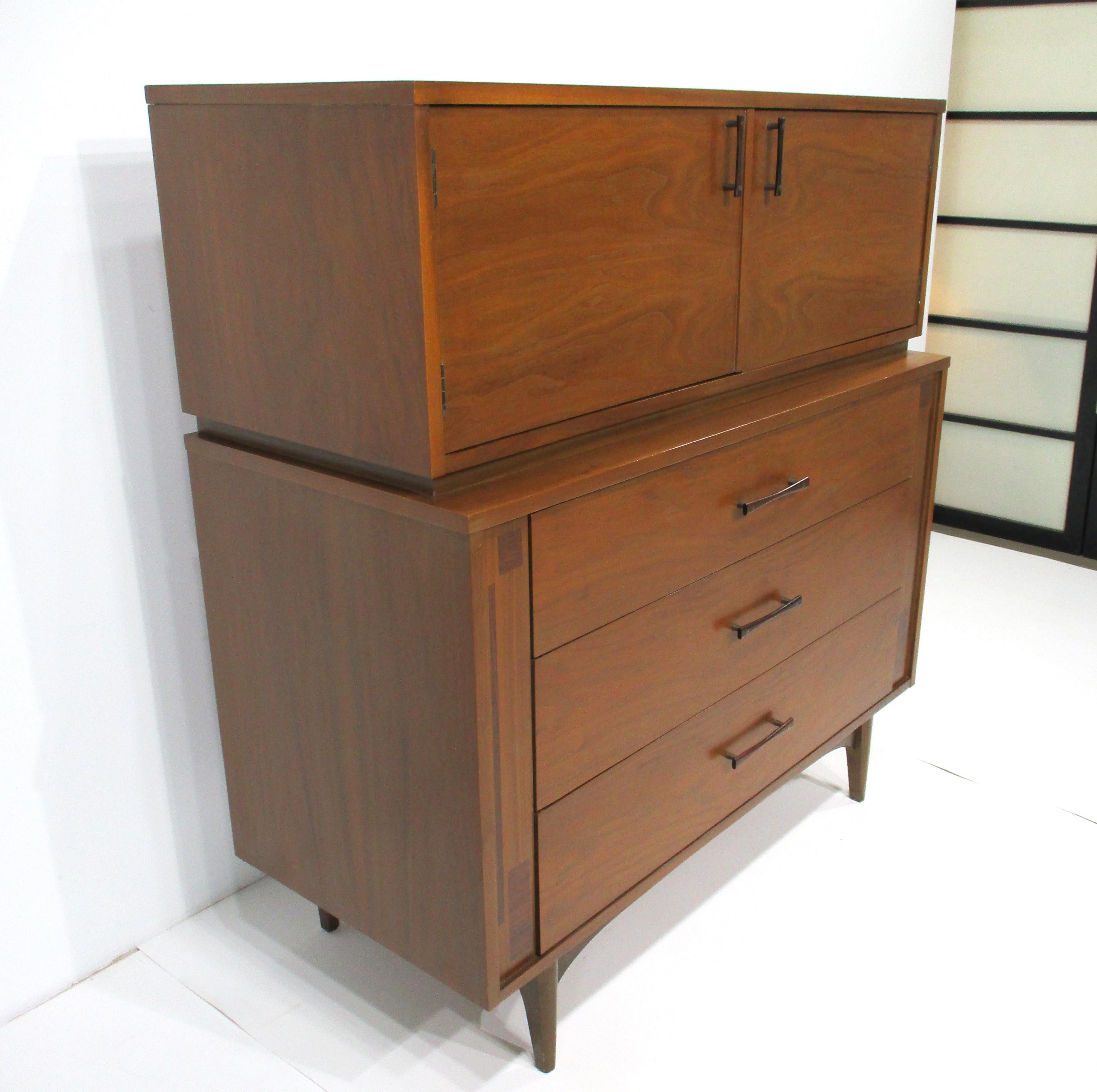 Cómoda highboy de nogal muy bien trabajada, con puertas superiores, dos cajones, uno de ellos con separadores, y tres zonas de almacenamiento muy funcionales para objetos doblados. Los tres cajones inferiores más grandes, uno de ellos con