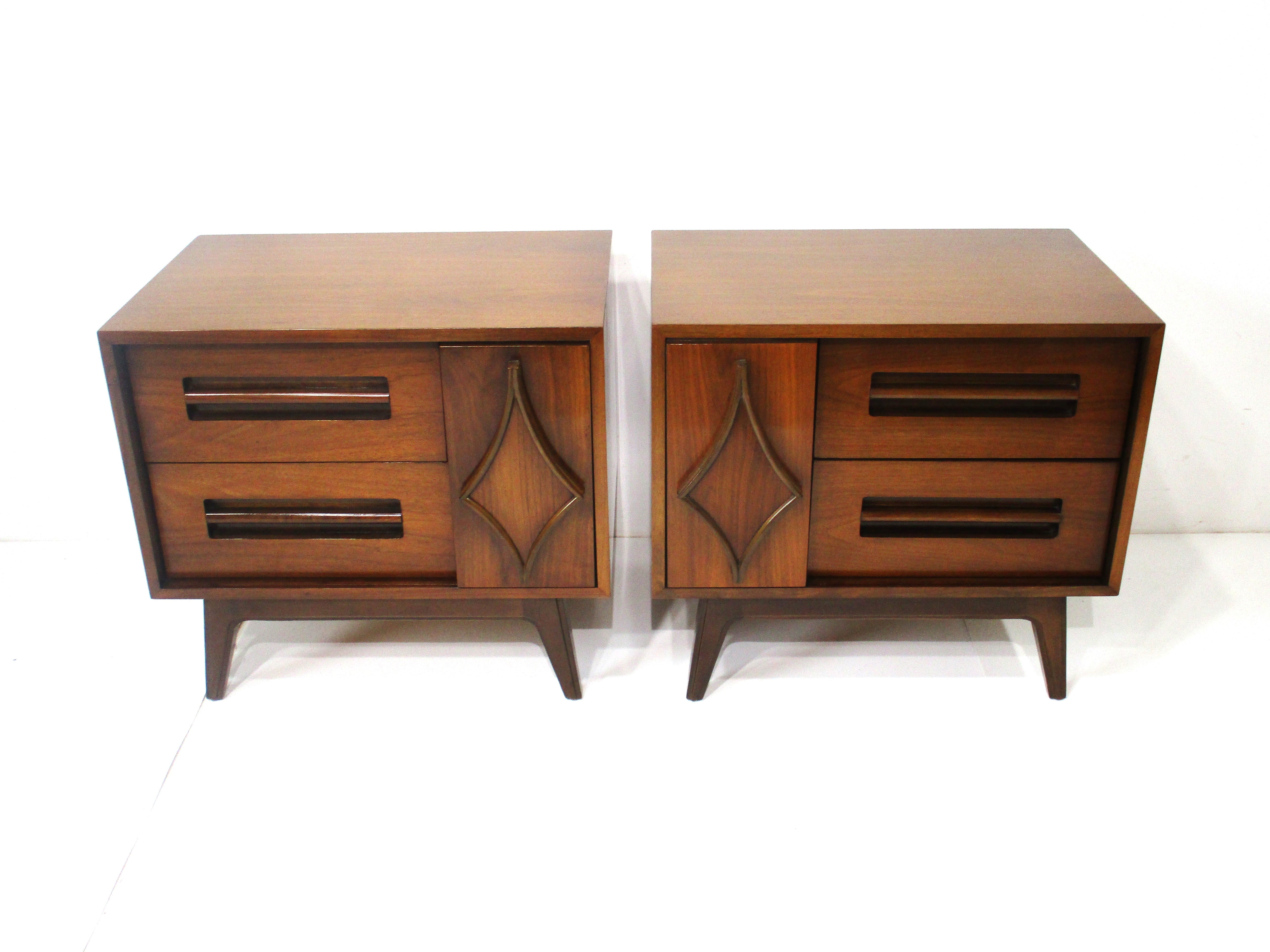 A pair of Mid Century walnut nightstands with a sliding door having a sculptural diamond designs to the front . Inside a storage area and to the other two drawers with built in long handles with grooved out finger pull to the bottoms for easy