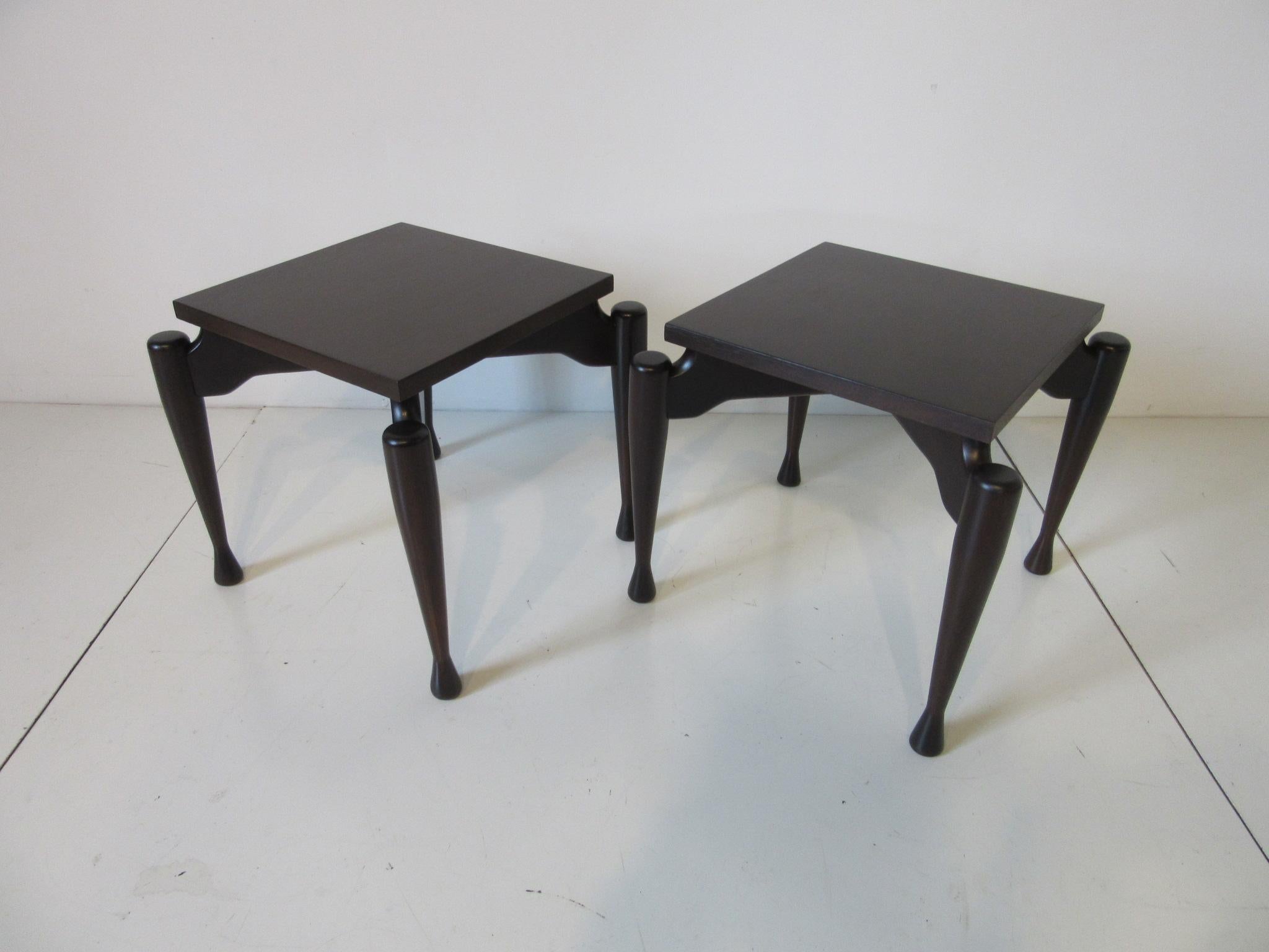 A pair of side or end tables with sculptural legs in a medium ebony finish with dark walnut tops in the Danish style.