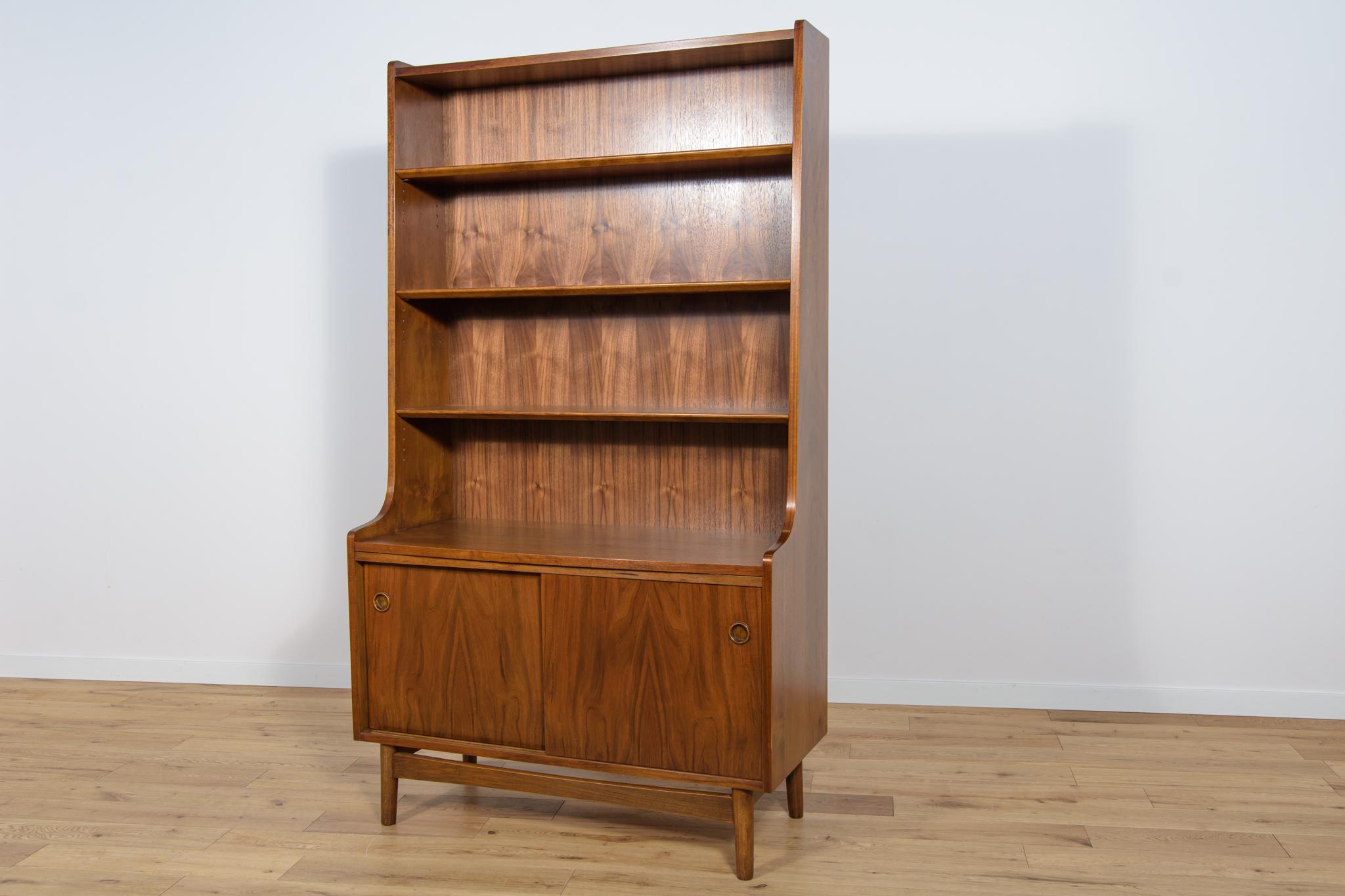 This Mid-Century Danish designed shelf was designed by Johannes Sorth and manufactured by Bornholms Møbelfabrik. It is made of walnut. In the upper part of the bookcase there are four shelves, in the bottom part there are a sliding door cabinet.