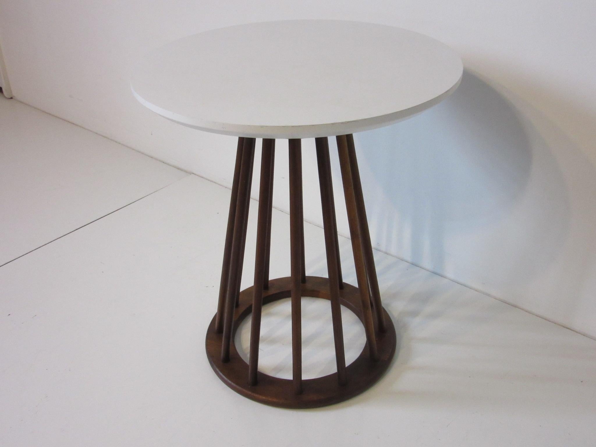 Dark walnut dowels make up the base for this side table designed by Arthur Umanoff attaching to the lower matching wood base with a white laminate top. The combination of wood and the white top bring together a softer modern midcentury look,