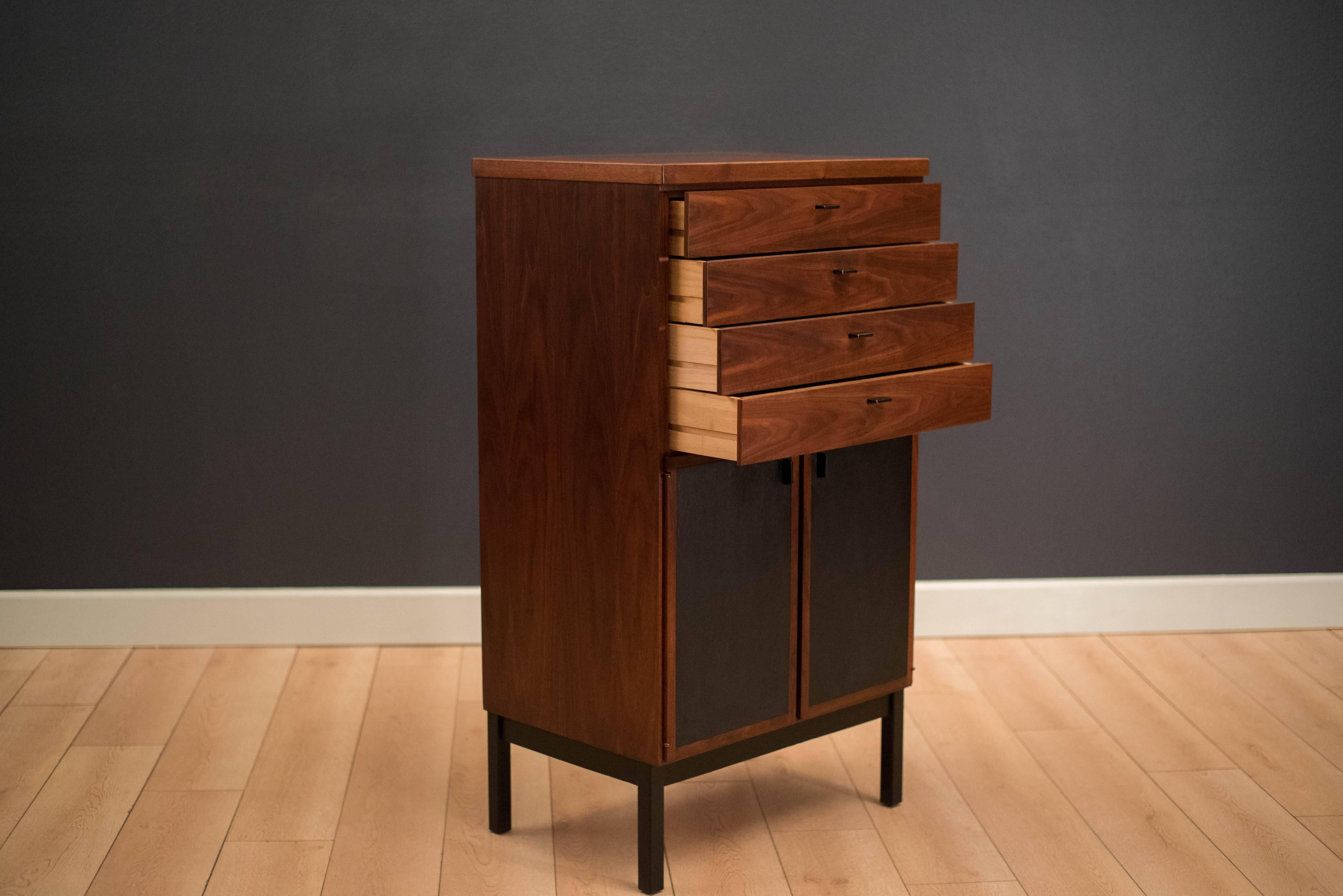 Mid-century modern tall dresser in walnut. This piece includes four dovetailed drawers with black metal pulls. Swing out doors are lined with black vinyl that reveal open storage space with one adjustable divider. Matching low dresser available in