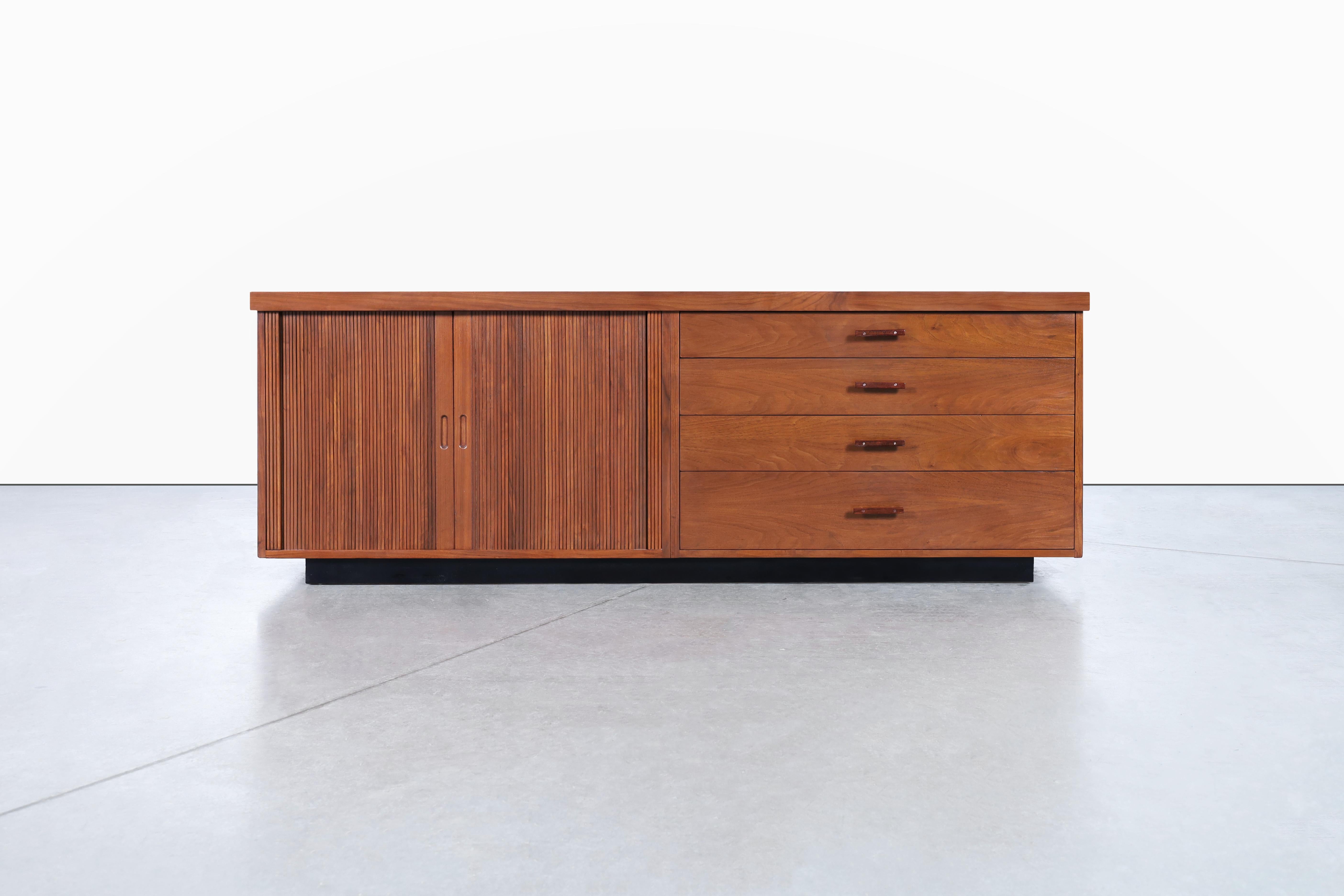 Mid-century walnut tambour door credenza manufactured by Glenn of California in the United States, circa 1950s. This storage unit boasts a stunning blend of functionality and aesthetics. It is crafted with premium quality walnut wood and features a