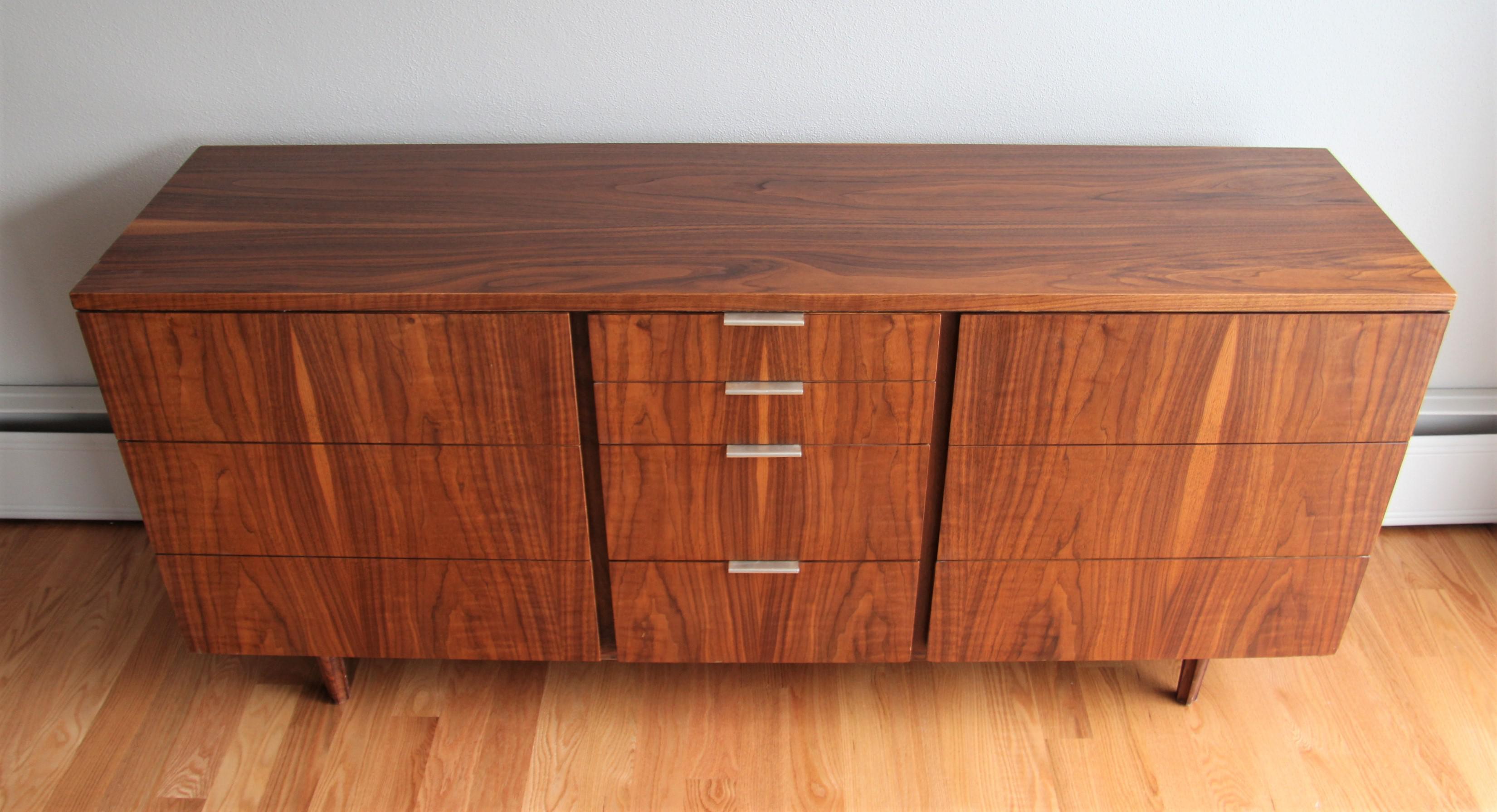 Mid-Century Modern bookmatched walnut triple dresser designed by John Stuart for Johnson Furniture Company. This piece boasts rich warm vibrant wood tones and superior craftsmanship. Plenty of storage with four center drawers flanked by banks of