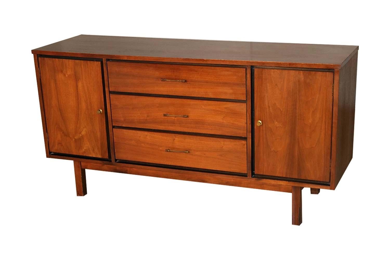 A fabulous Classic Mid-Century Modern walnut triple dresser or sideboard. Featuring a beautifully grained walnut wood case and ebonized frame housing three center drawers, each drawer is adorned with a single bow tie pull creating a striking