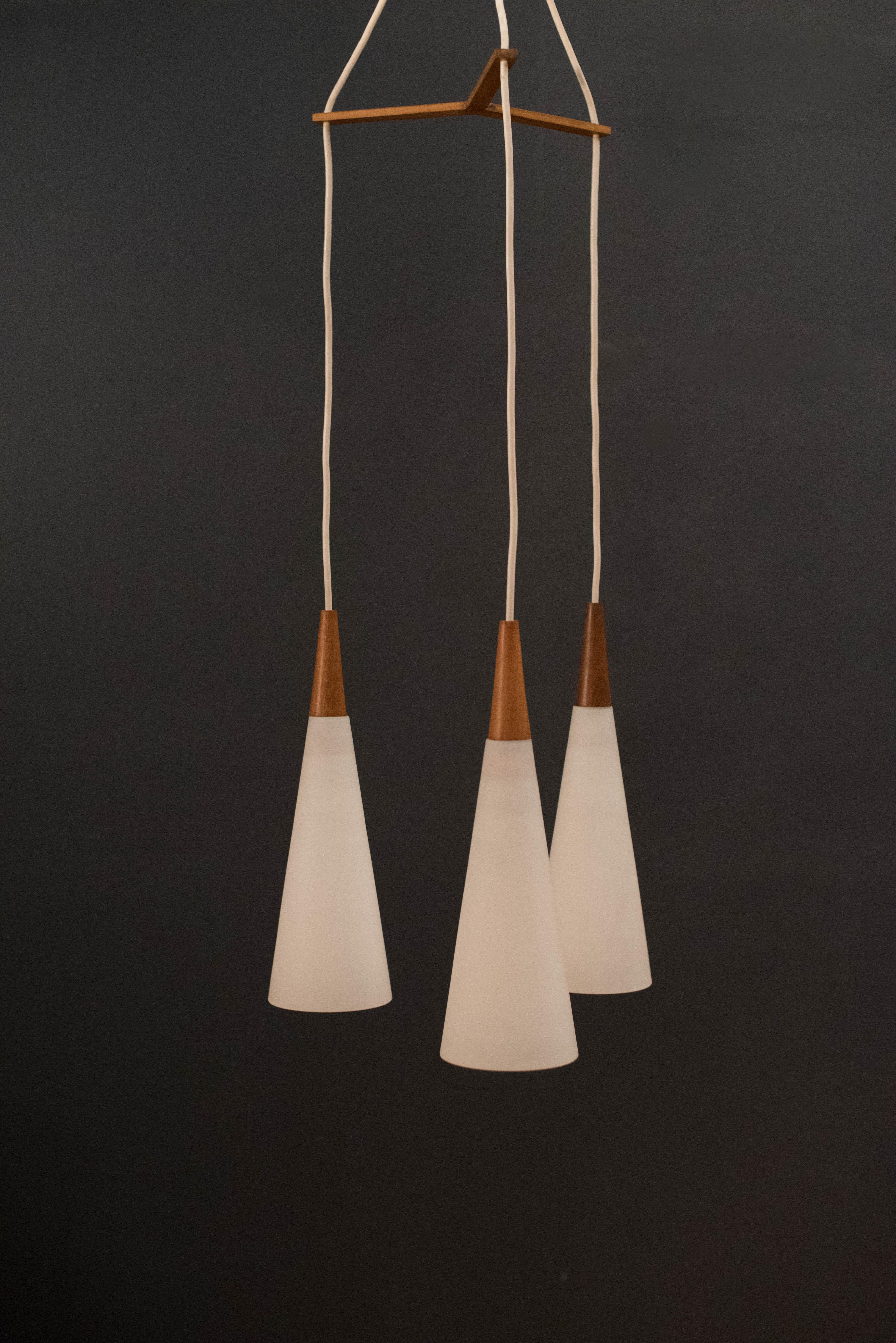 Vintage triple hanging pendant lamp, circa 1960s. This piece includes three frosted glass cone lights with walnut accents. 

Pendant: 5