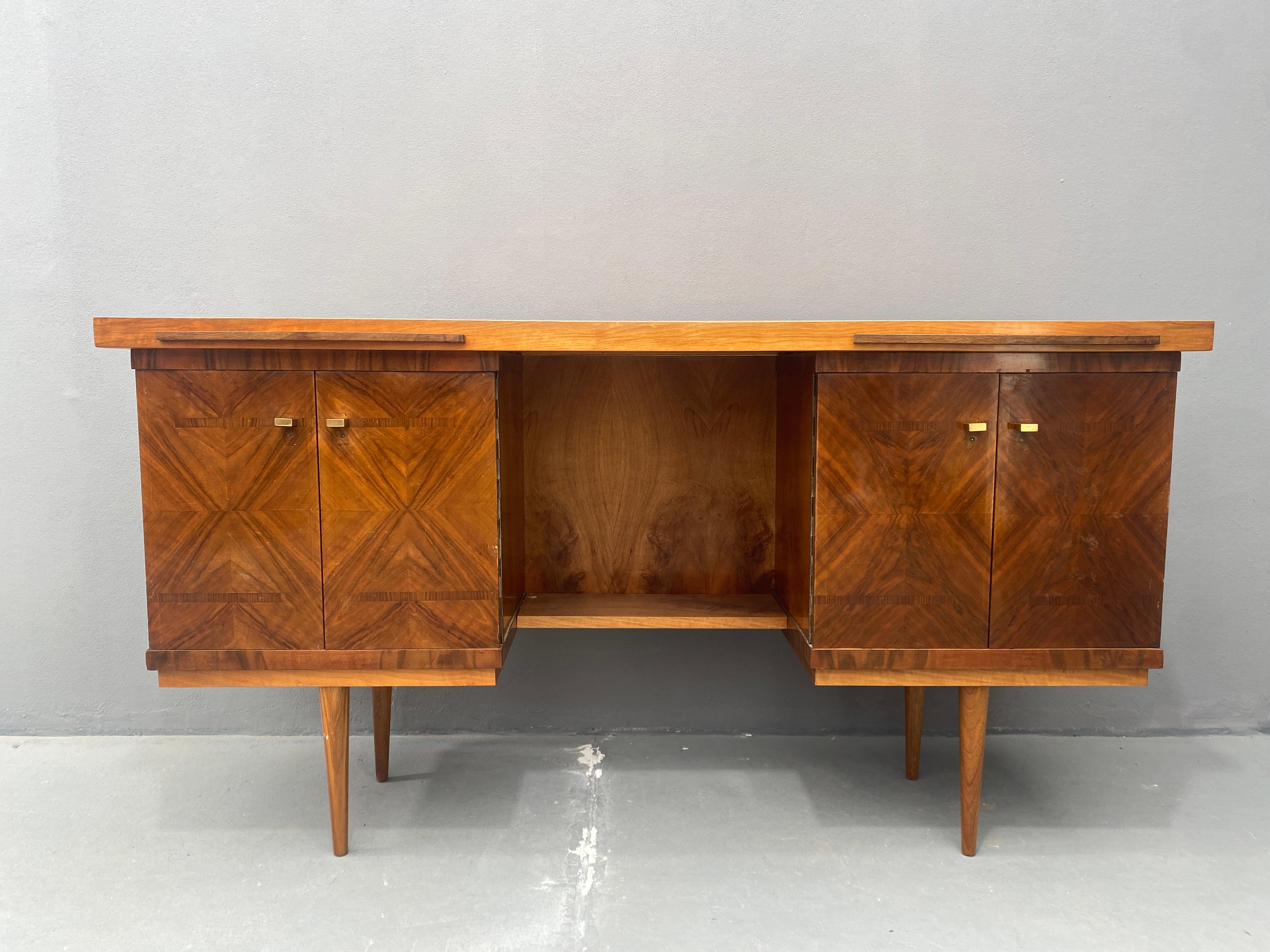Ce long bureau avec une belle surface en placage de noyer a été fabriqué dans l'ancienne Tchécoslovaquie dans les années 1970. Il comprend deux armoires ornées d'un motif symétrique en bois et de petites poignées en laiton. La partie centrale est
