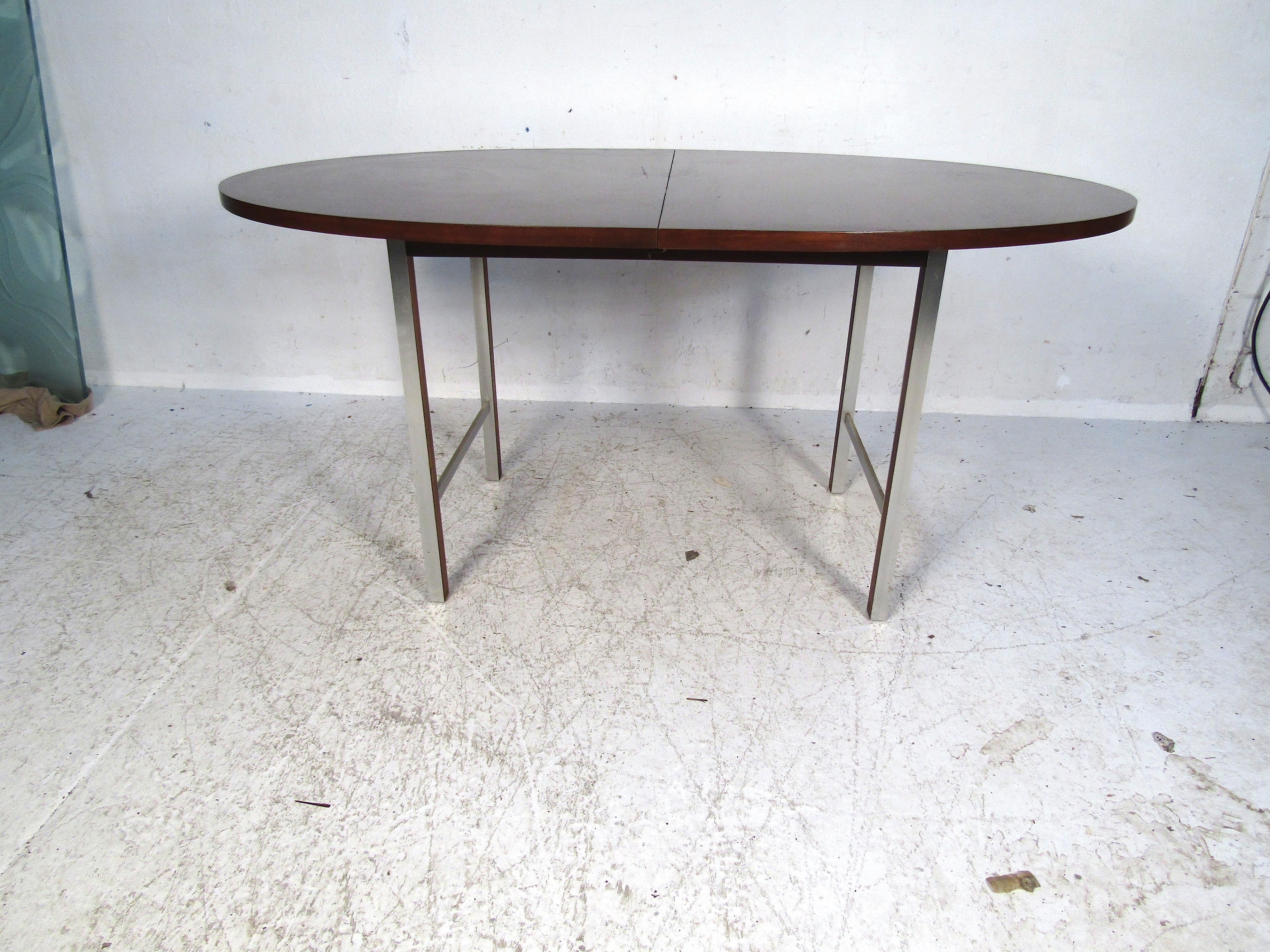 This midcentury dining table is simplistic in design, but still quite elegant. It features a deep color with beautiful grain patterns. The legs feature subtle chrome accents with walnut inlays. Perfect for a large kitchen or smaller dining room.
