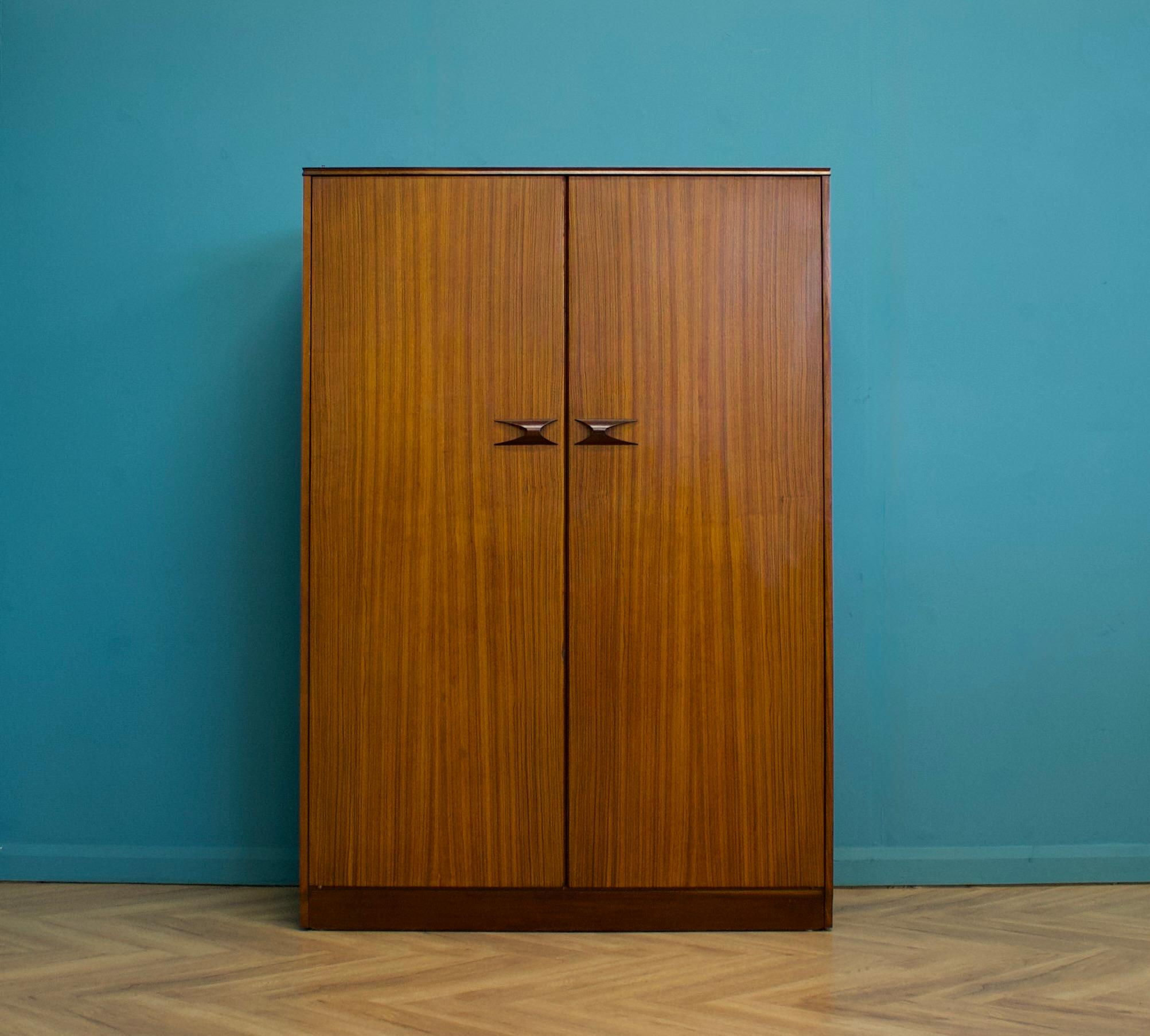 Ein freistehender zweitüriger Kleiderschrank aus zebranofurniertem Holz, hergestellt von Elliots of Newbury in den 1960er Jahren.




Er zeichnet sich durch seine Schwalbenschwanzgriffe aus Palisanderholz aus und ist mit einer Kleiderstange in