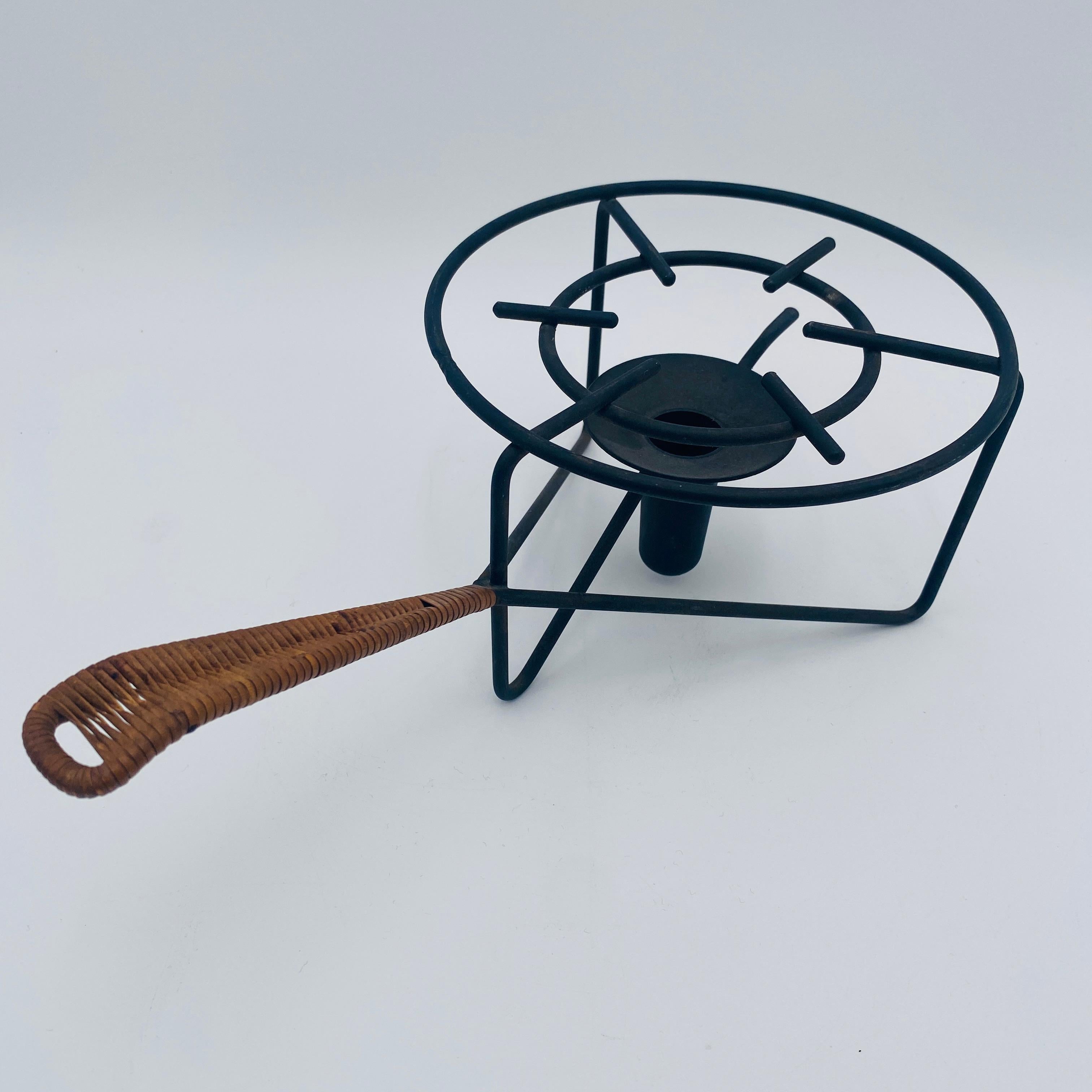 Un icónico soporte de calentamiento moderno de mediados de siglo diseñado y fabricado por Laurids Lønborg en Dinamarca durante la década de 1960. Está realizada en hierro ennegrecido y cuenta con un asa decorativa y práctica de ratán. Está destinado