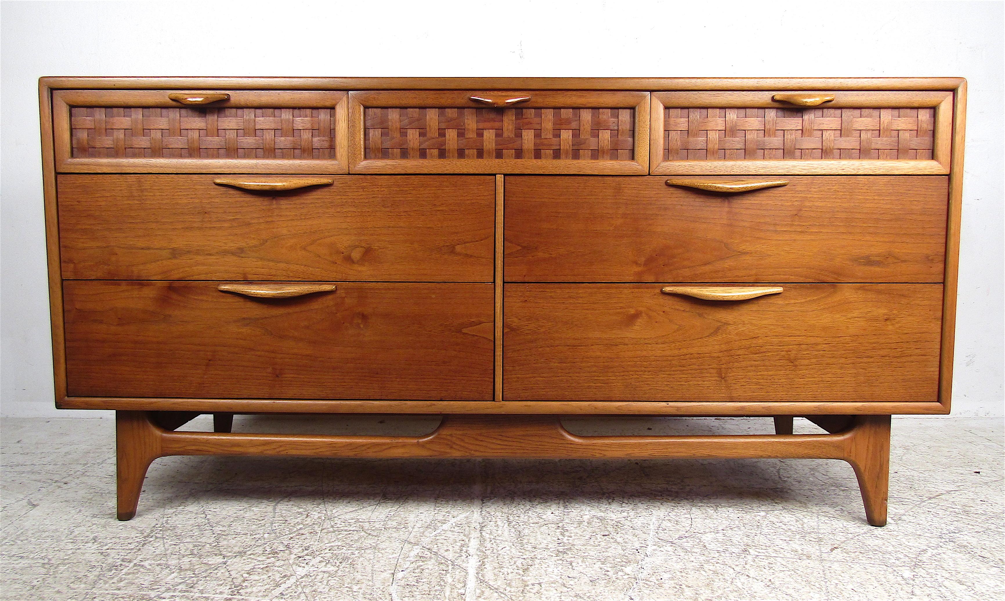 This beautiful vintage walnut dresser by Lane boasts three top drawers with woven fronts. A sculpted base with tapered legs and a stretcher ensures maximum sturdiness without sacrificing style. The unique carved drawer pulls and straight lines add