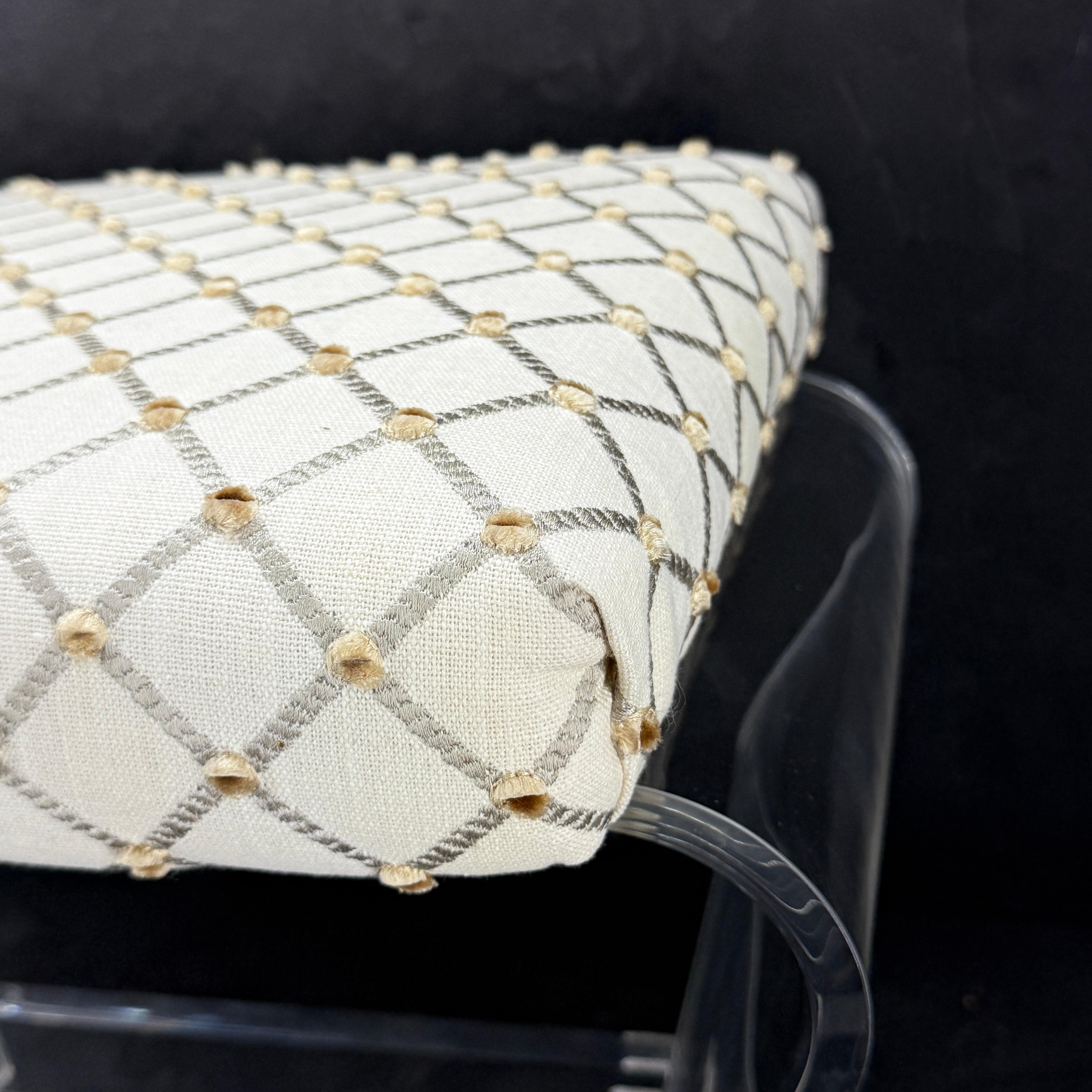 This bench or stool features thick lucite with a waterfall design newly upholstered in a neutral linen patterned fabric. The bench, which features a center bar, would make it well suited as a vanity stool. This stool is newly upholstered.