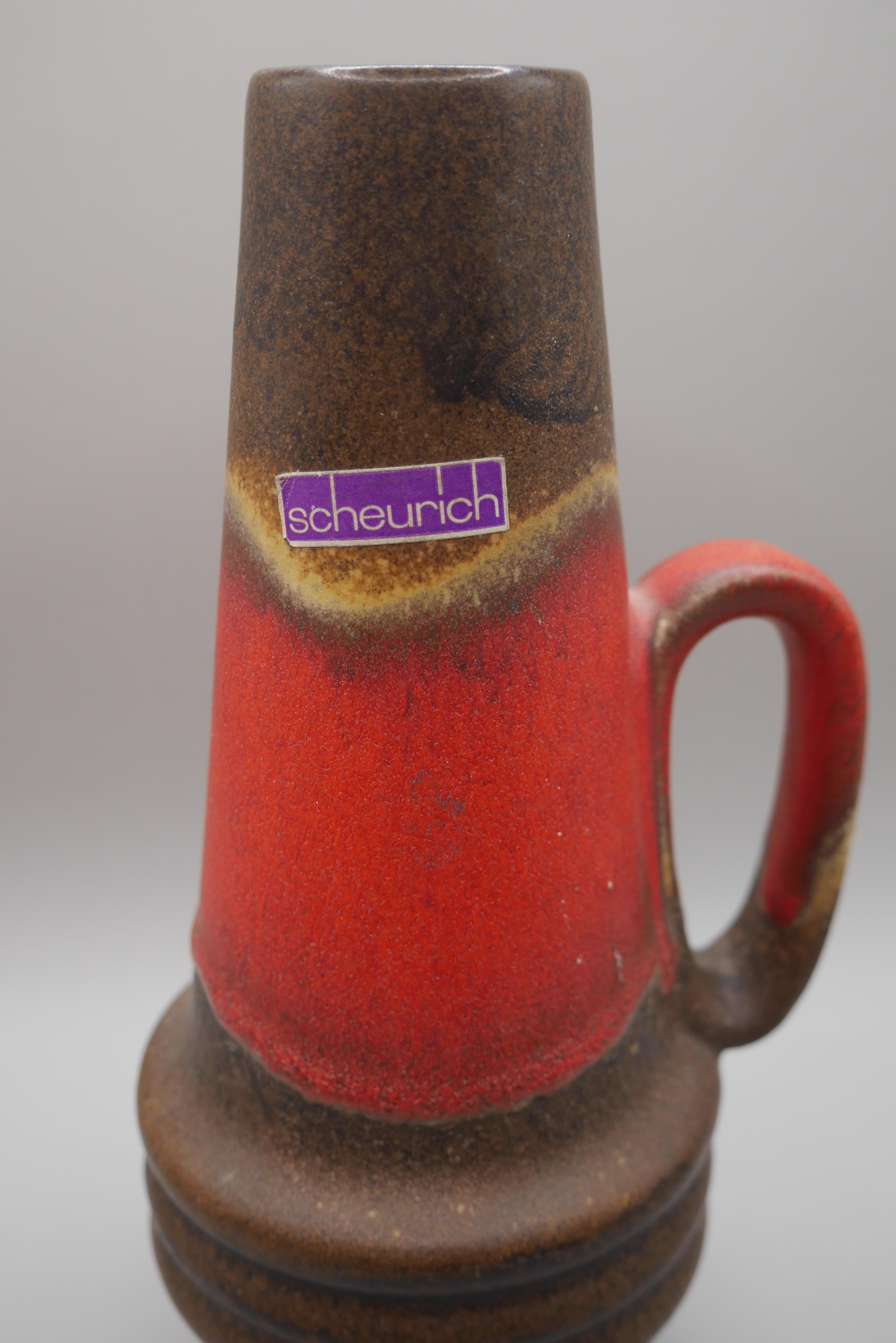 A lovely, handled vase from Scheurich, West Germany with a red and dark brown glaze. 

Alois Scheurich and his cousin Fridolin Greulich started in 1928 a wholesale company in glass, porcelain and ceramics in Schneeberg, Germany. In 1948 they