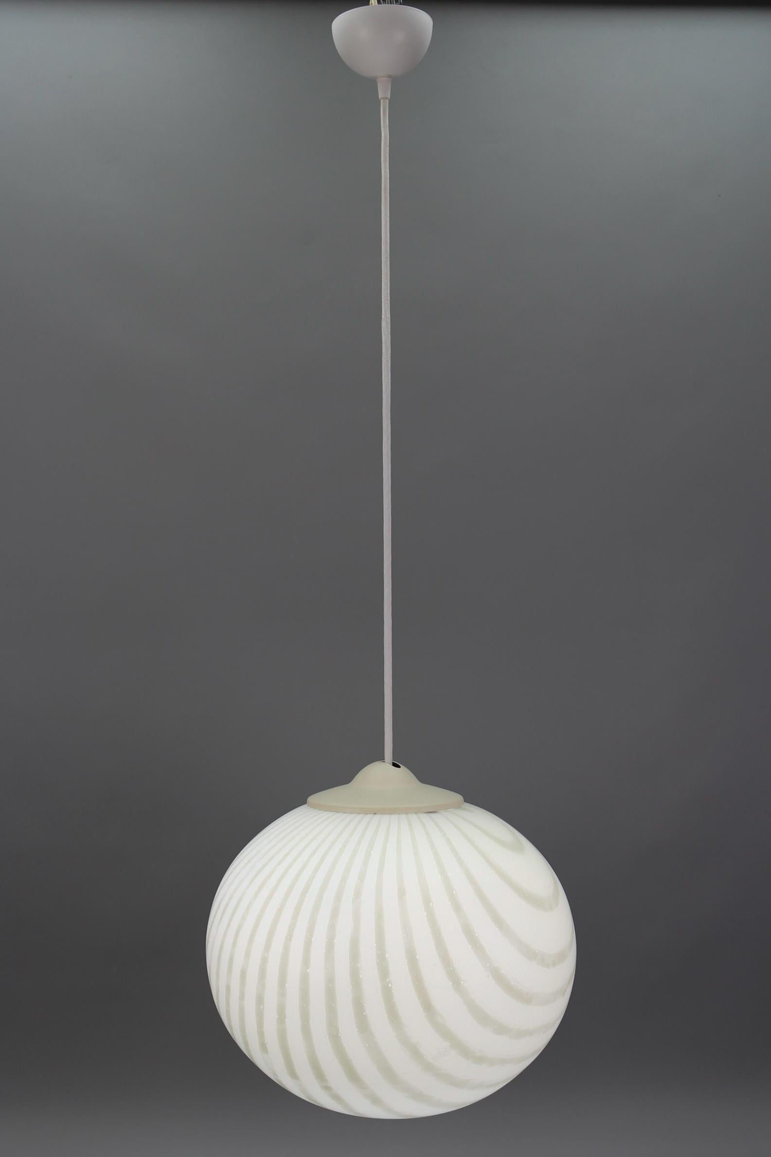 Lámpara colgante globo de cristal a rayas blancas y color crema de Peill & Putzler, Alemania, hacia la década de 1970.
Esta impresionante lámpara colgante tiene un globo de cristal opalino soplado a mano con rayas de color blanco y crema. Los