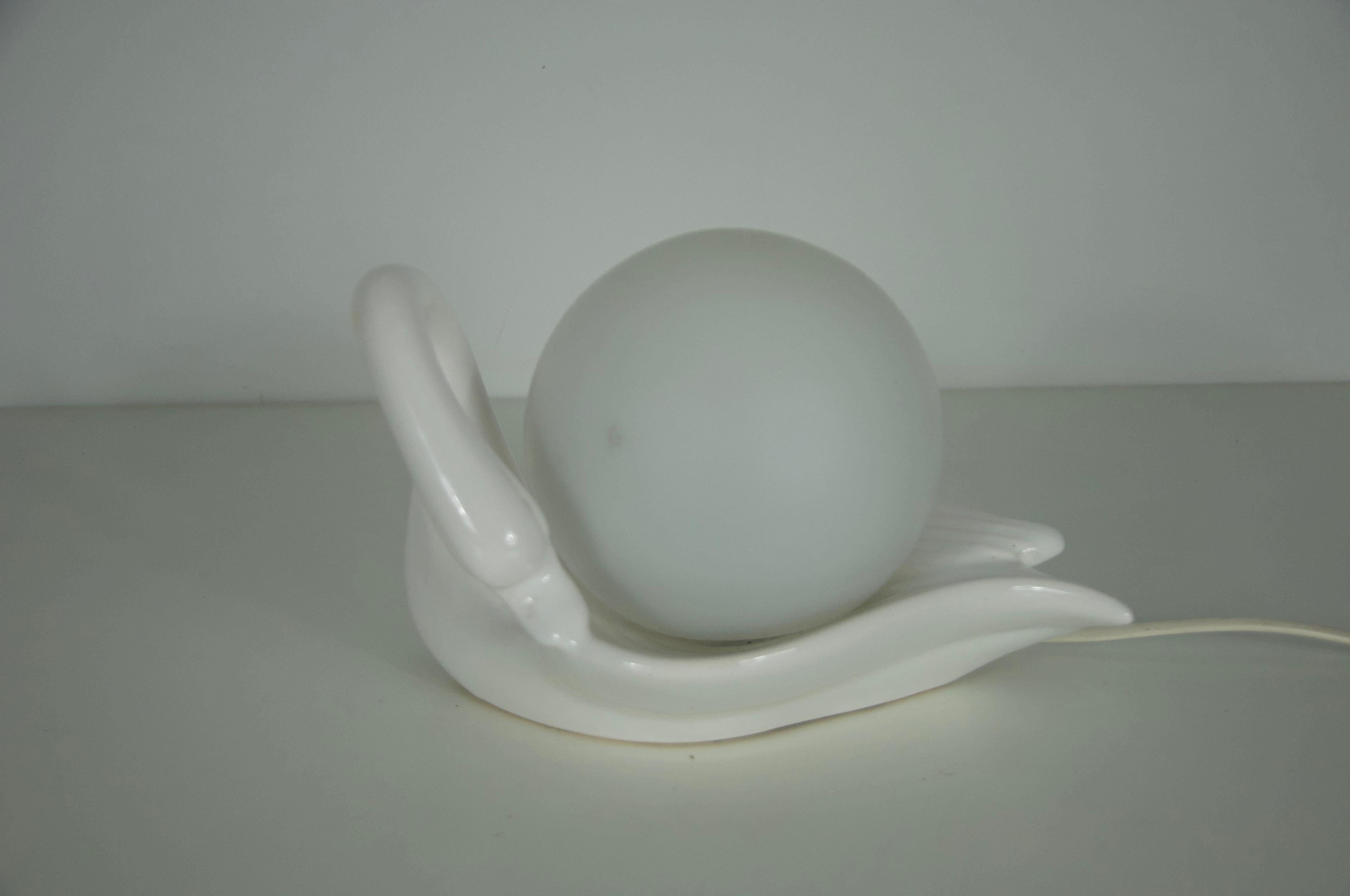 Esta elegante lámpara de sobremesa italiana de los años 60 muestra las cualidades escultóricas del diseño cerámico de mediados de siglo. Realizada en cerámica blanca brillante, la base adopta la forma de un cisne estilizado, que sostiene con gracia
