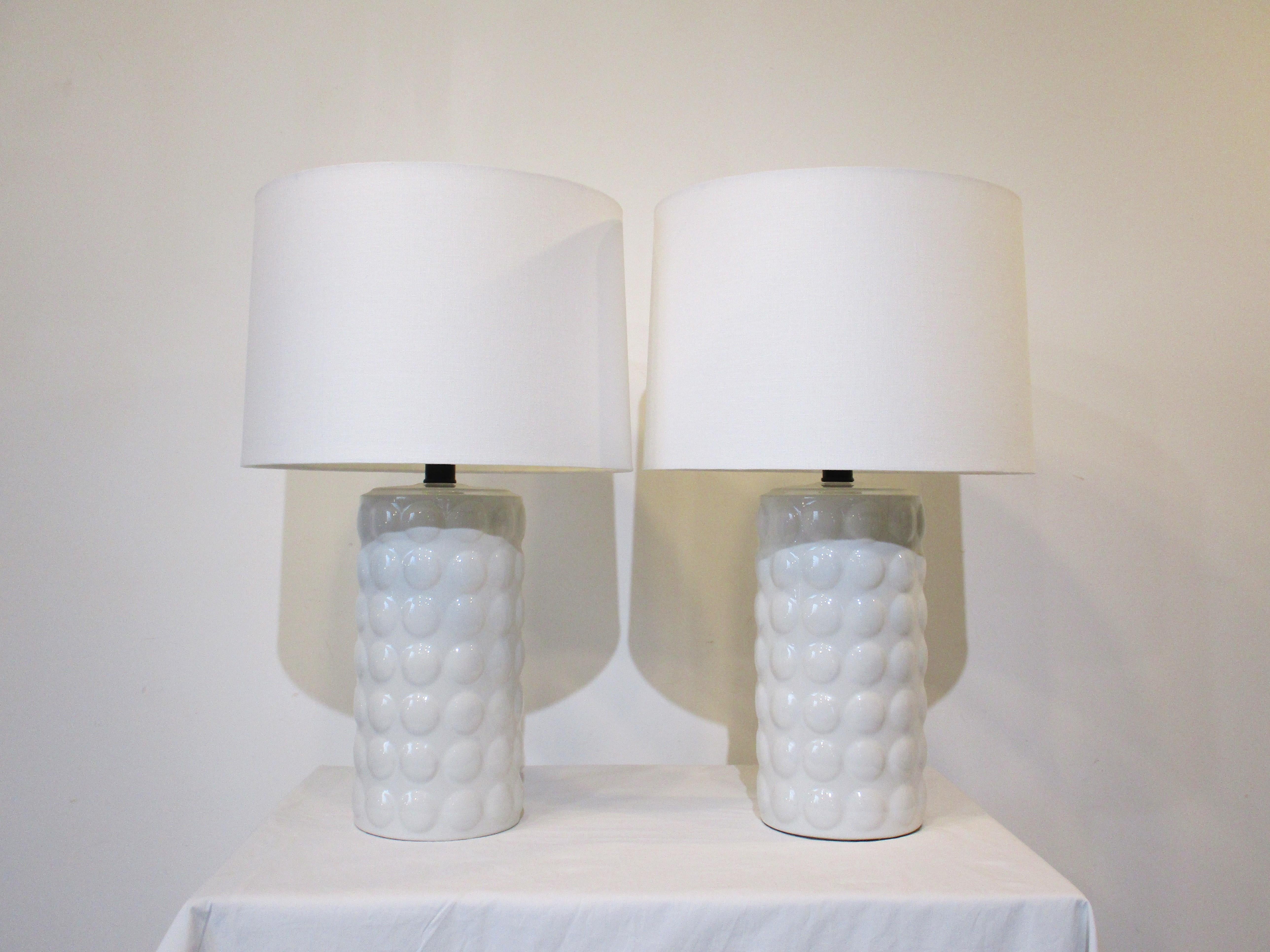 A wonderful pair of white ceramic table lamps with ball design to the bases and topped with cream linen shades . Manufactured in the manner of the Chapman Lighting company, very well crafted and has that simple but sophisticated rich look and feel.