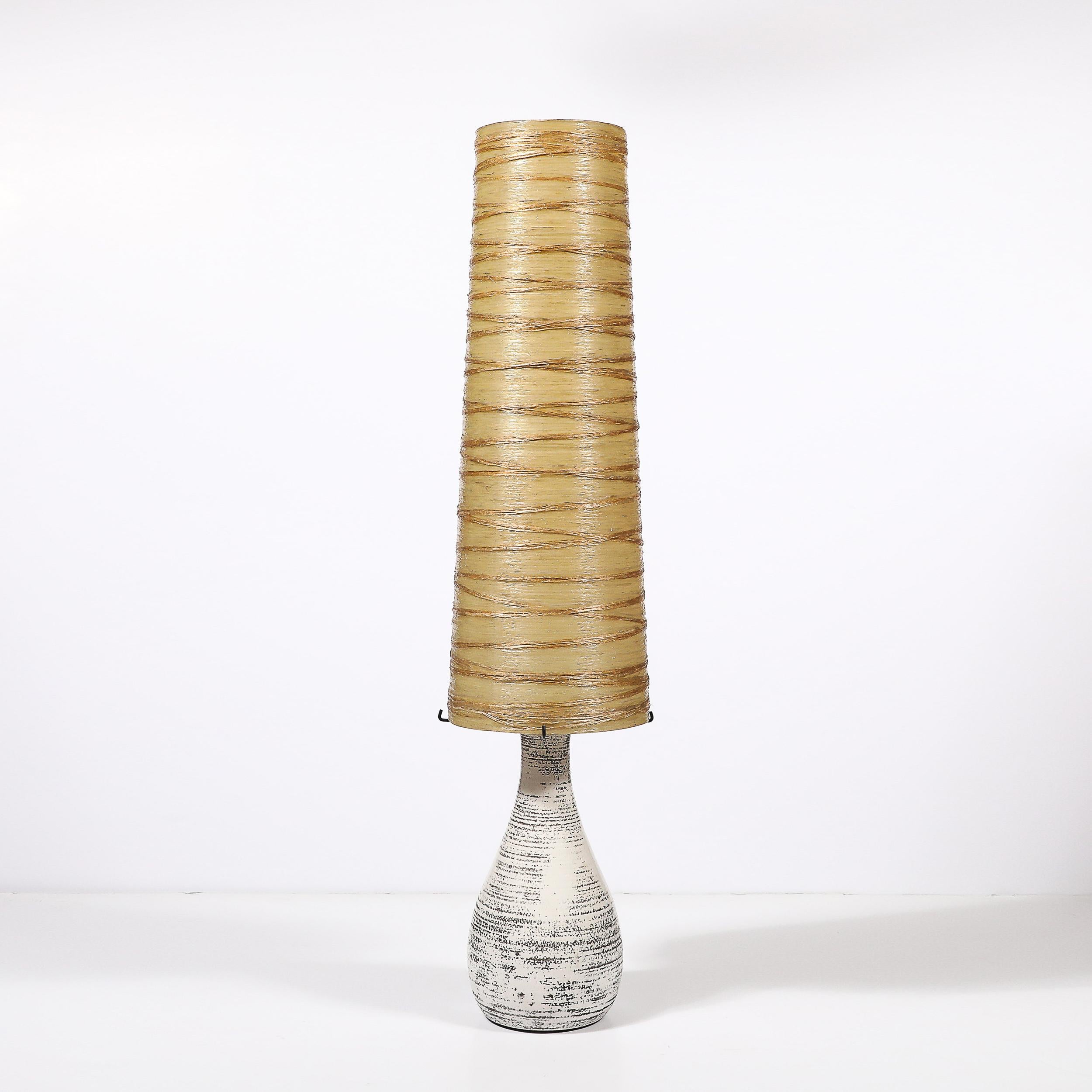 Cette lampe de table moderniste du milieu du siècle, fabriquée en France vers 1950, présente un mélange harmonieux de matériaux et de contrastes audacieux. La base est en céramique émaillée blanche avec des détails texturaux organiques émaillés