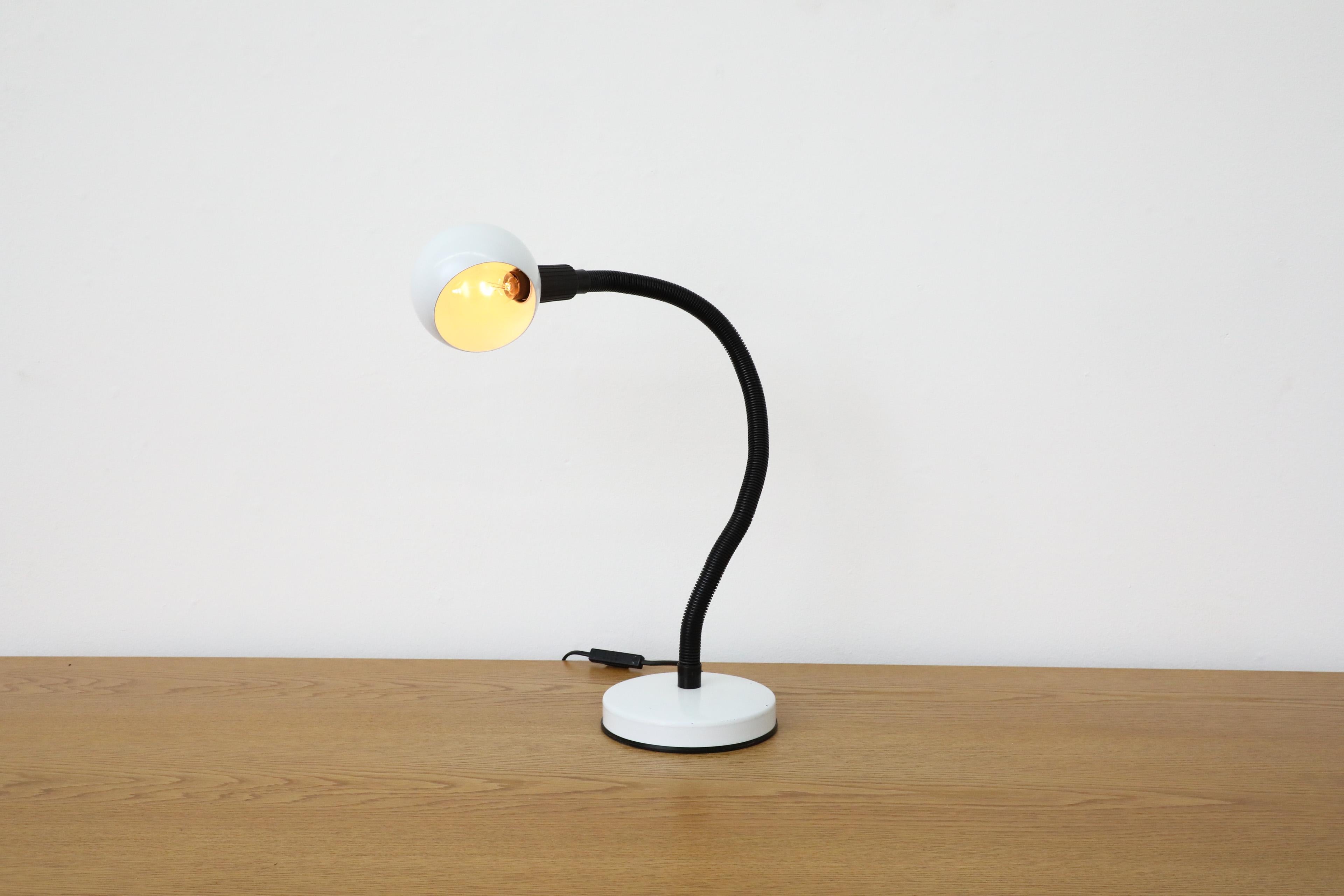 Mid-Century gooseneck globe desk lamp with white enameled metal base and globe and posable black stem. Black and red toggle switch on cord. European E14 candelabra bulb socket. In original condition with wear consistent with age and use.
