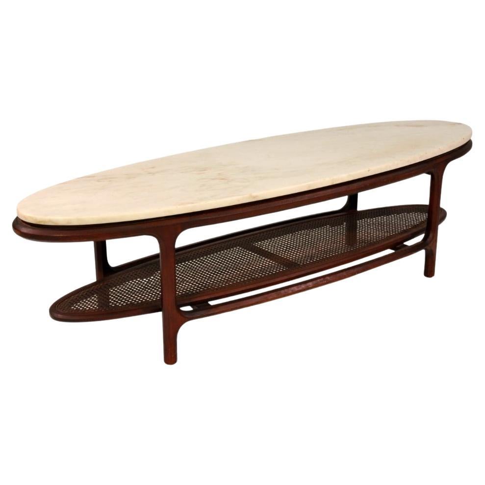 All original, vintage two-tier surfboard cocktail table with off-white Italian marble top and caned magazine shelf. Circa 1950s. Manufactured by Gordon's Inc. of Johnson City, Tennessee. One owner table; original finish.