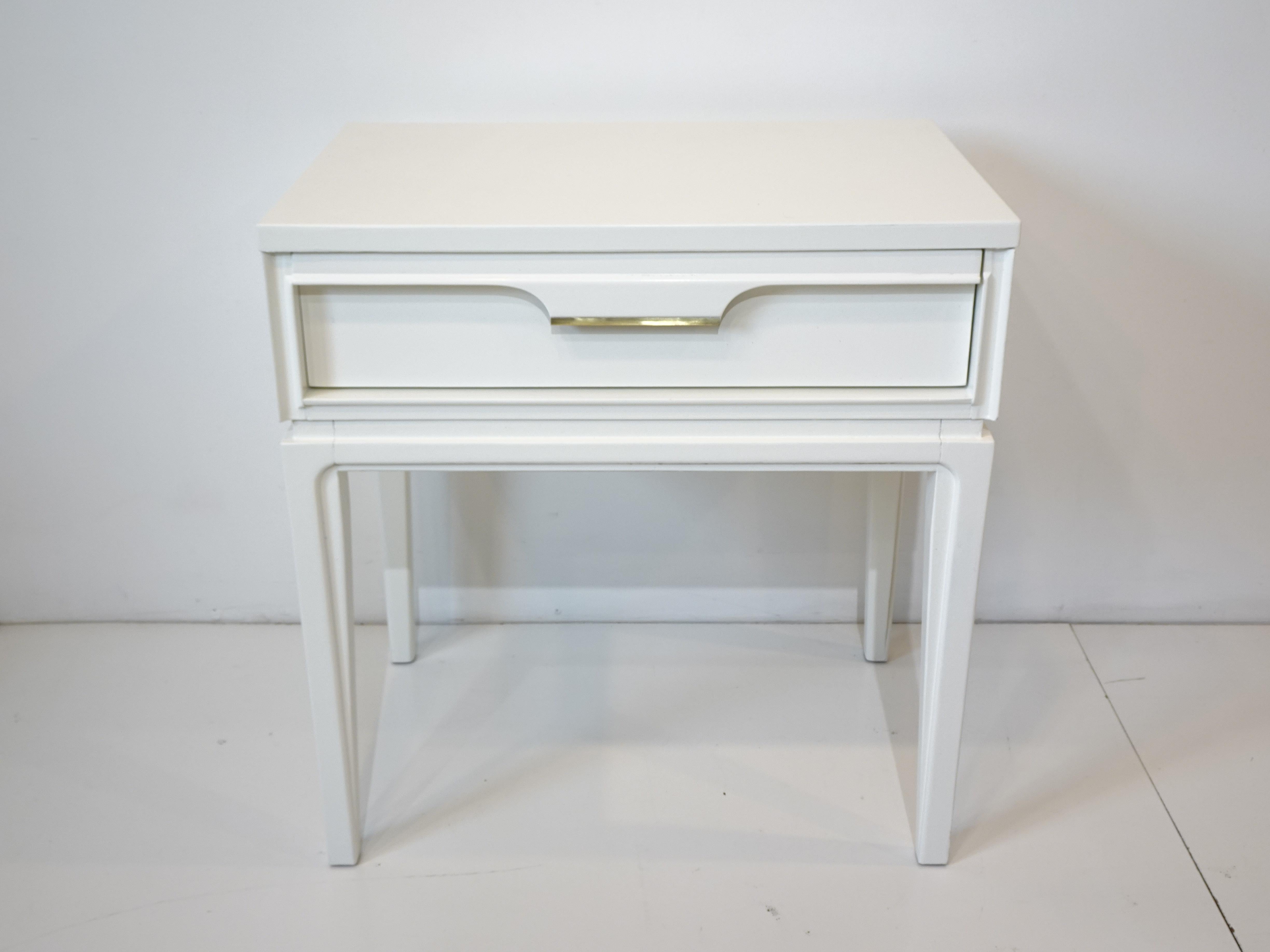 A simple satin white Mid Century one drawer nightstand with detailed trim and brass giving the piece a nice tailored look manufactured by the Basic Witz Furniture company.