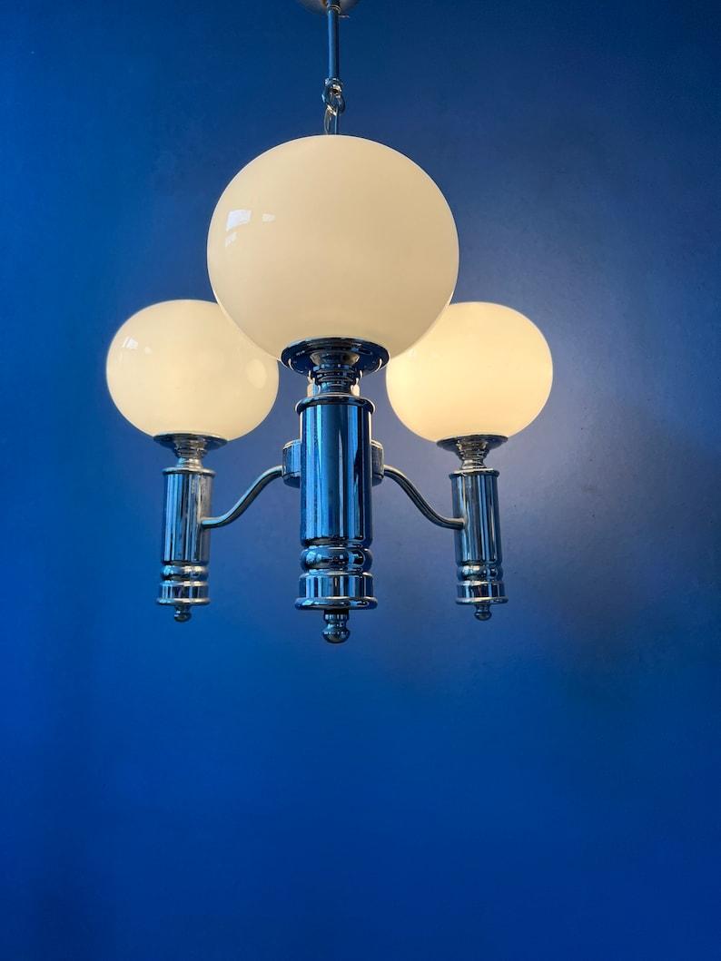 Lovely opaline milk glass chandelier with shiny chrome frame. The lamp requires three E14 lightbulbs.

Additional information:
Materials: Glass, metal
Period: 1970s
Dimensions:ø Full lamp: 38 cm
Height (adjustable): 69 cm
Condition:Very good. Both
