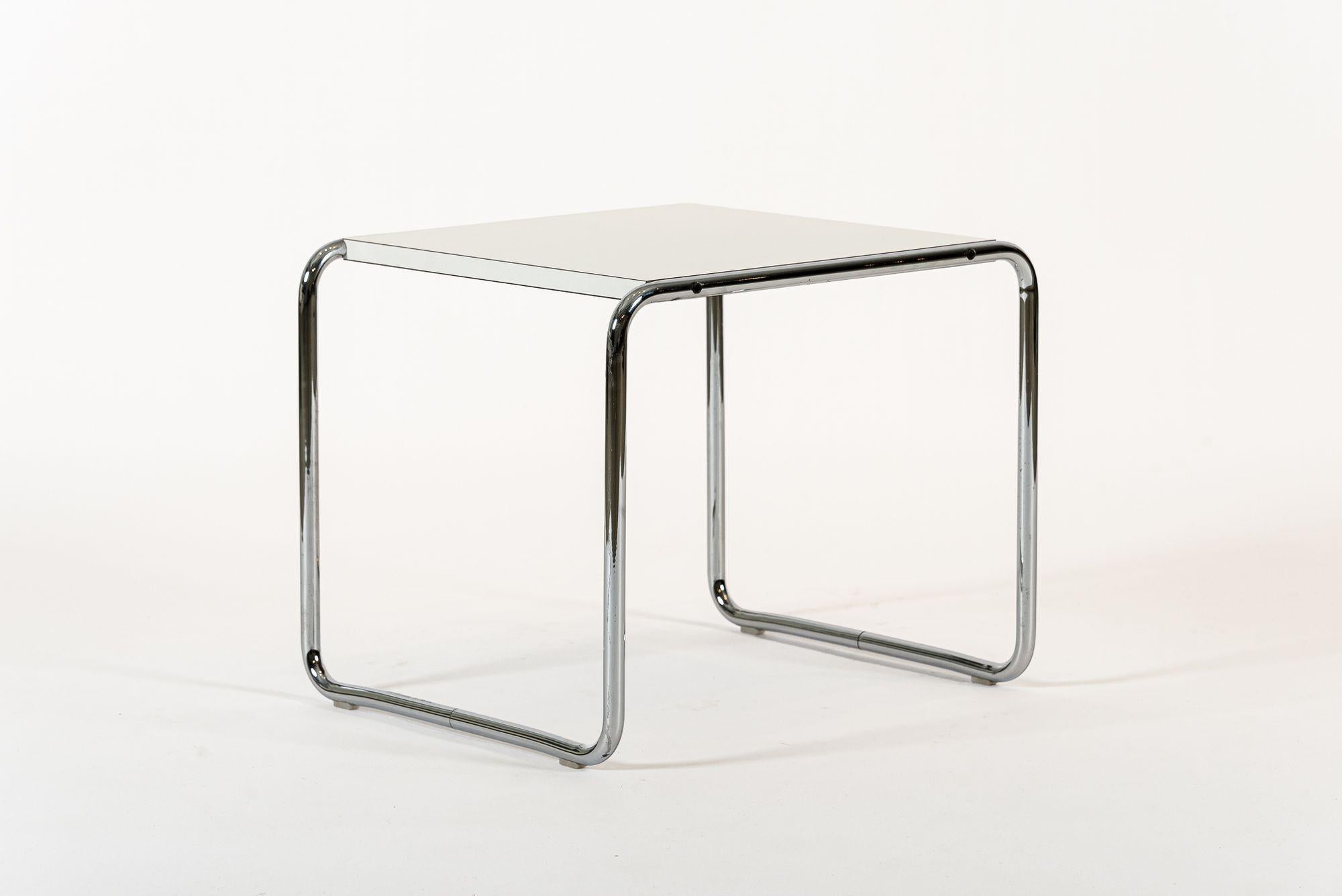 This mid century modern rectangular Laccio side or end nesting table was designed by Marcel Breuer in 1924 and manufactured by Knoll circa 2000s. The classic design features a polished chrome tubular steel frame with a white, satin finish laminate