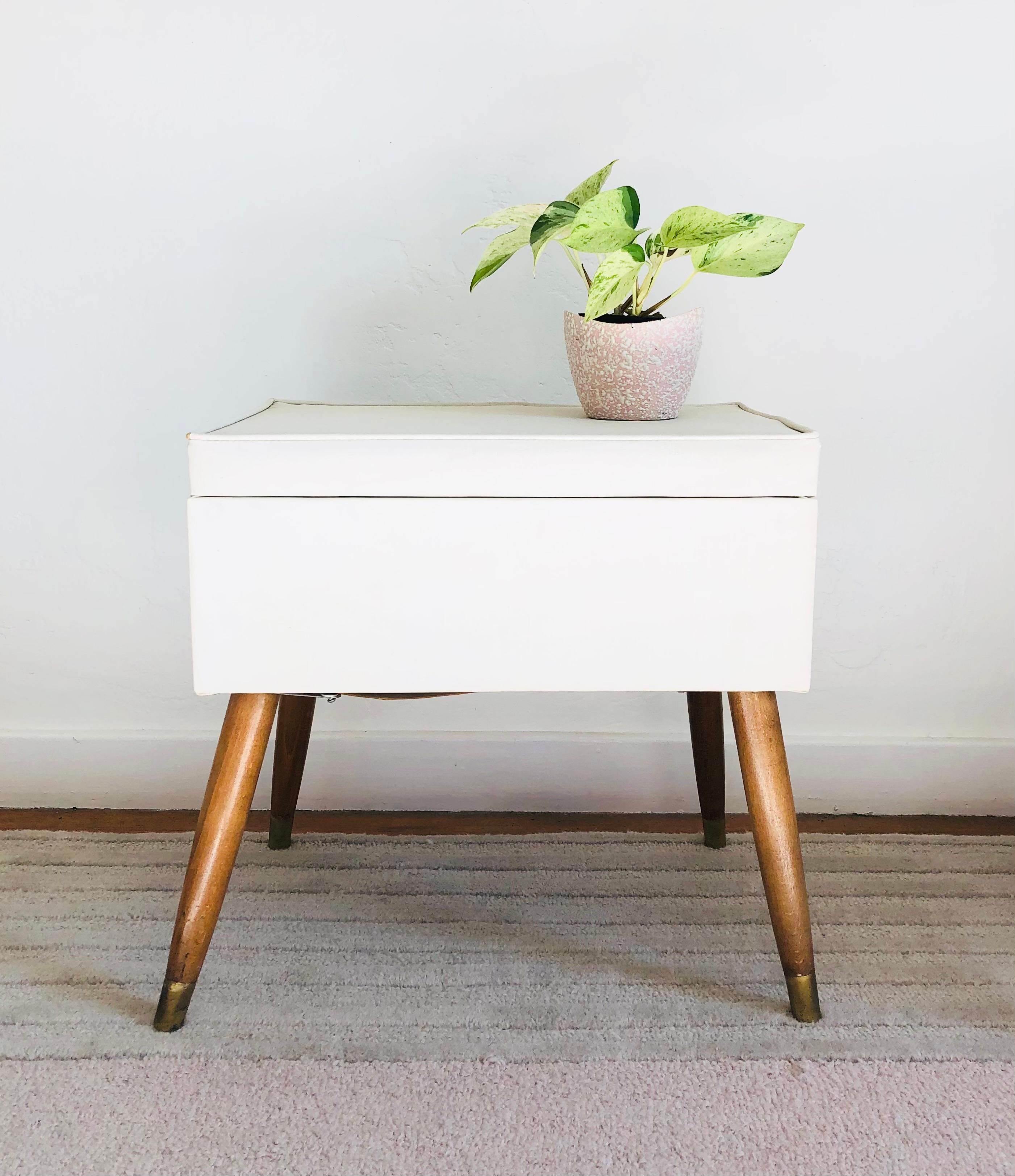 A mid-century vinyl stool with storage. Stands on tapered wood legs. The top hinges open to reveal a roomy interior for storing items. Legs will be unscrewed for shipping.
 