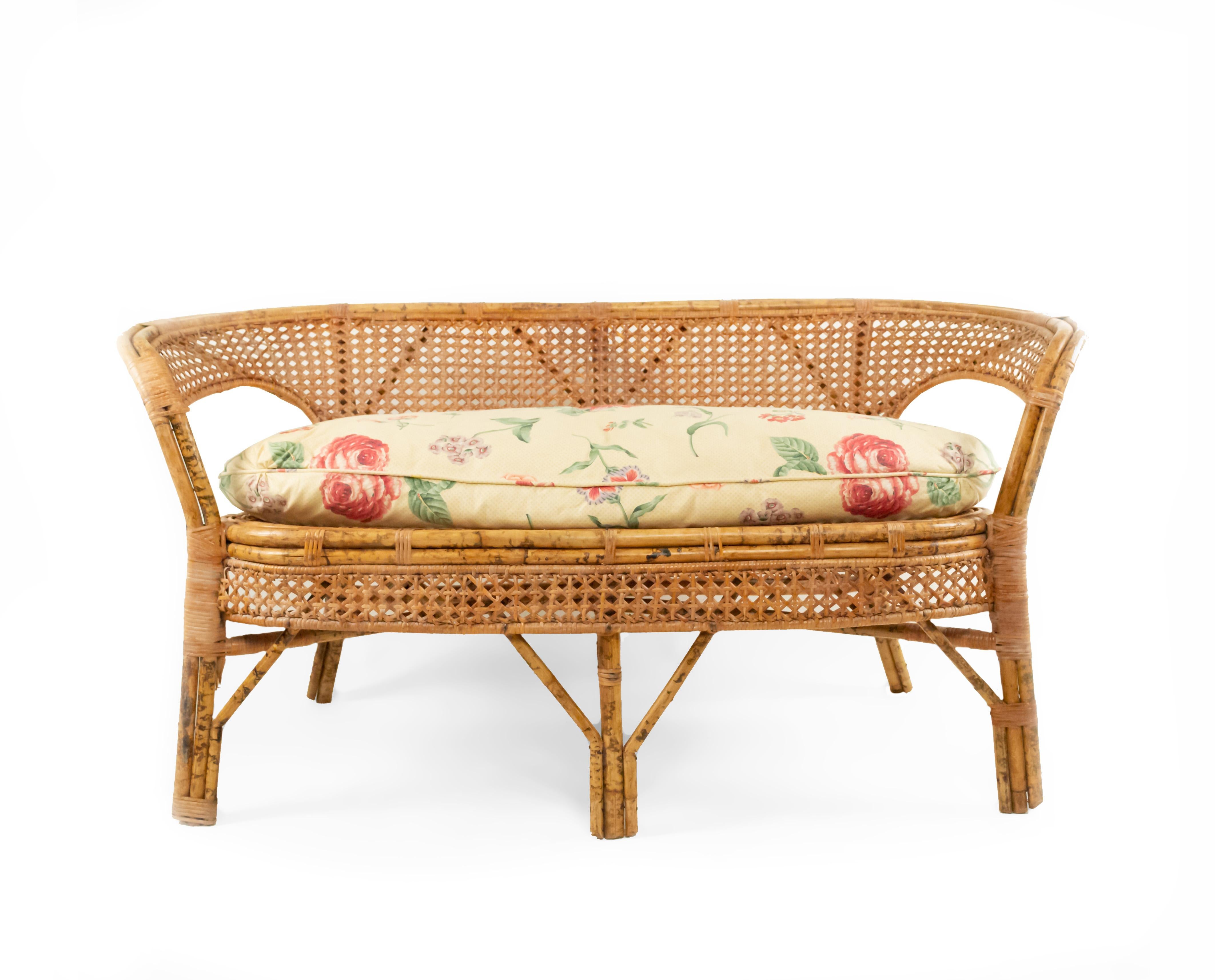 American midcentury wicker love seat with rounded back arms and cane panels with a floral upholstered cushion (circa 1950s-1960s).