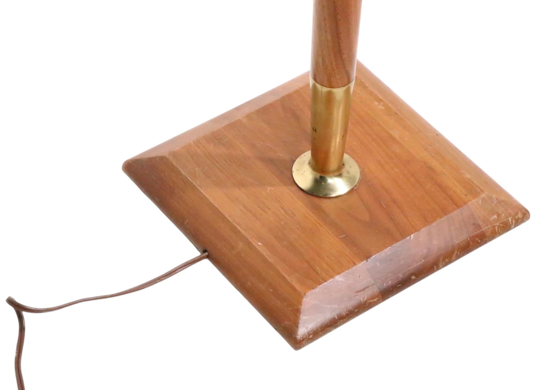 Stylish Mid Century floor lamp constructed of walnut and brass, in clean, original, working condition The lamp features an elegant elongated center pole, with a candlestick like top, mounted on a square base. Design reminiscent of Gerald Thurston,