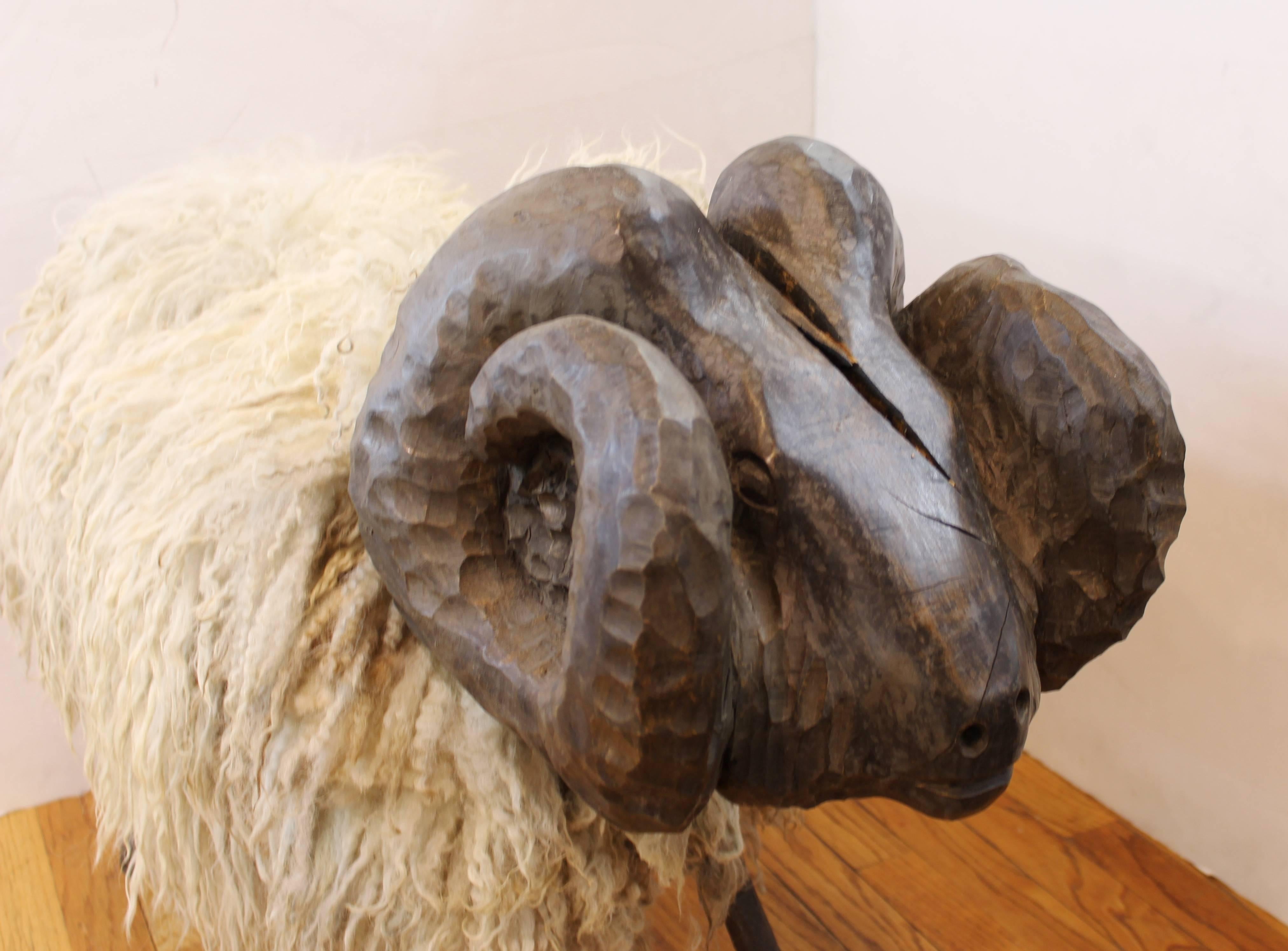 A midcentury sheep sculpture, with a metal and wood structure and its original sheepskin. The head has a large crack on the front. The wool shows signs of age and wear.