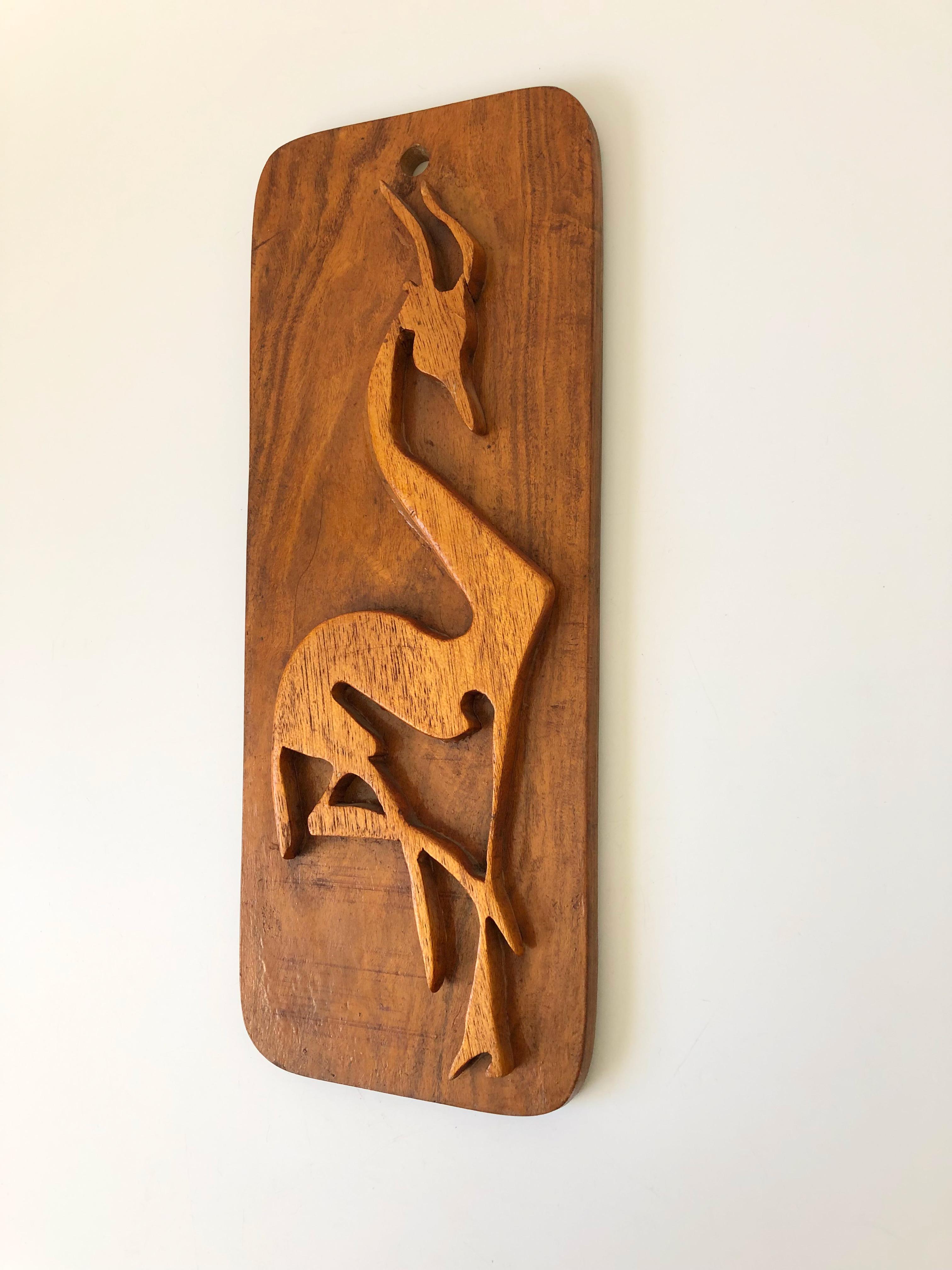 A mid-century wood wall hanging with a carved wood gazelle in the center. Great stylized form. A hole is formed on the top for hanging.
 
