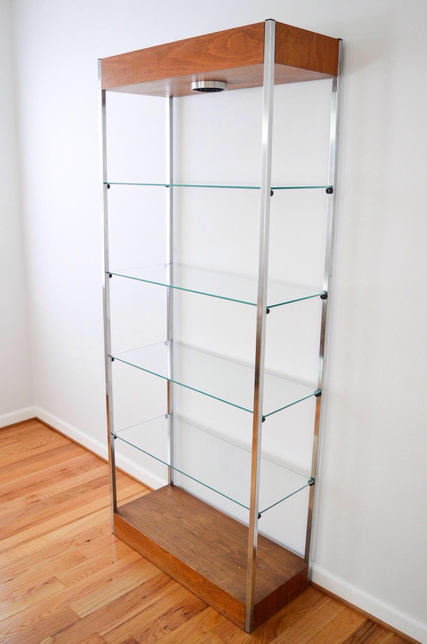 • Striking Mid-Century Modern lighted etagere or shelving unit, circa 1960.
• Classic modern minimalism with an elegant form and clean lines.
• Aluminum frame with a tall wood header and footer.
• Four removable glass shelves plus bottom wooden