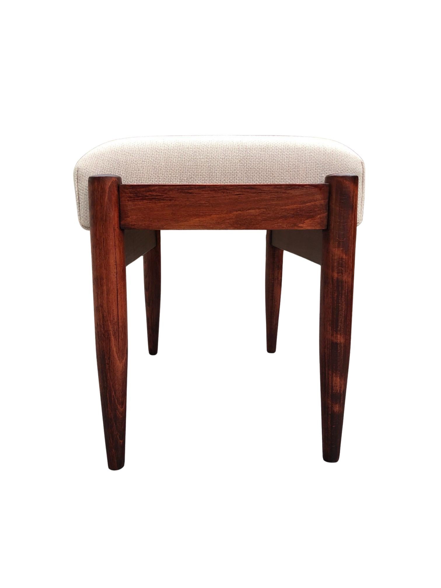 A comfortable stool, designed by Edmund Homa, manufactured by Goscinska Furniture Factory in Poland in the 1960s. 

The structure is made of solid beechwood in a warm color, finished with a semi matte varnish. The upholstery is made of a high