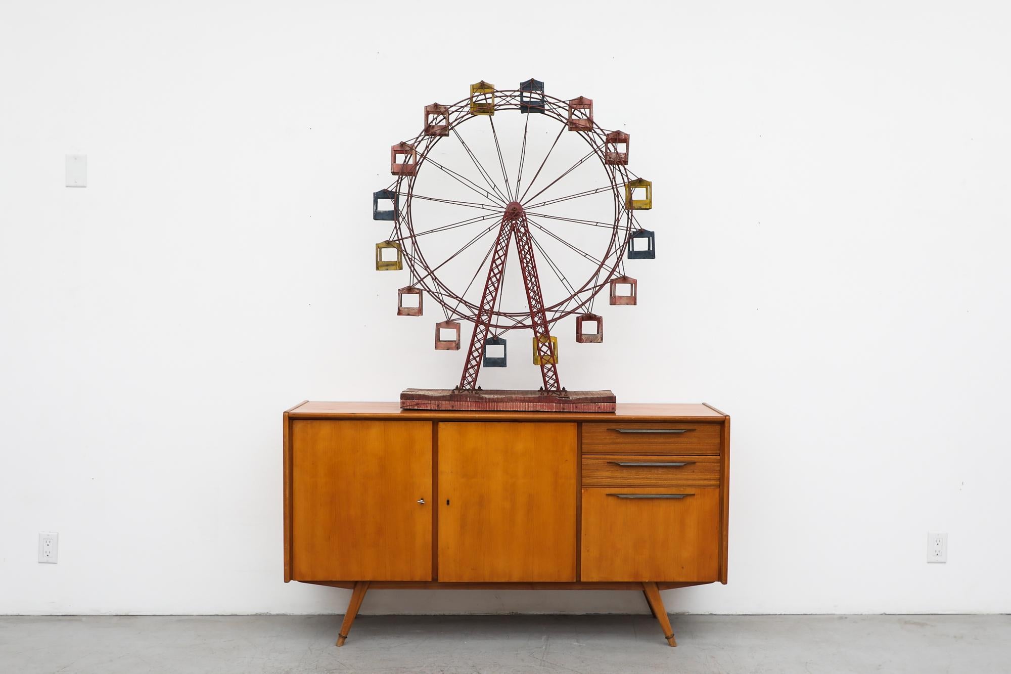 Fun Mid-Century Ferris Wheel with red enameled metal frame and wooden cabins mounted on a wooden block. The wheels spins and the little cabins move as well. In original condition with visible wear and patina, including some loose welds and hand