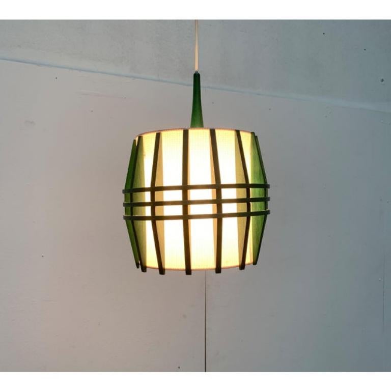 Ciondolo in legno di metà secolo di colore verde.

Il corpo della lampada è formato da una struttura a coste finemente lavorata, rivestita all'interno da un materiale traslucido. Gli anelli paralleli al centro vengono inchiodati alle costole e li