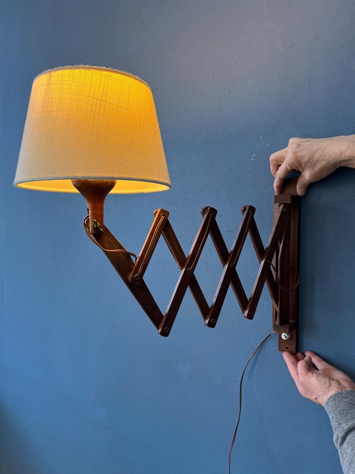 Danish style teak wood scissor lamp with wooden frame and beige textile shade. The scissor-mechanism allows you to extend the lamp from the wall. The shade itself can be adjusted too. The lamp requires an E27/26 (standard) lightbulb and currently