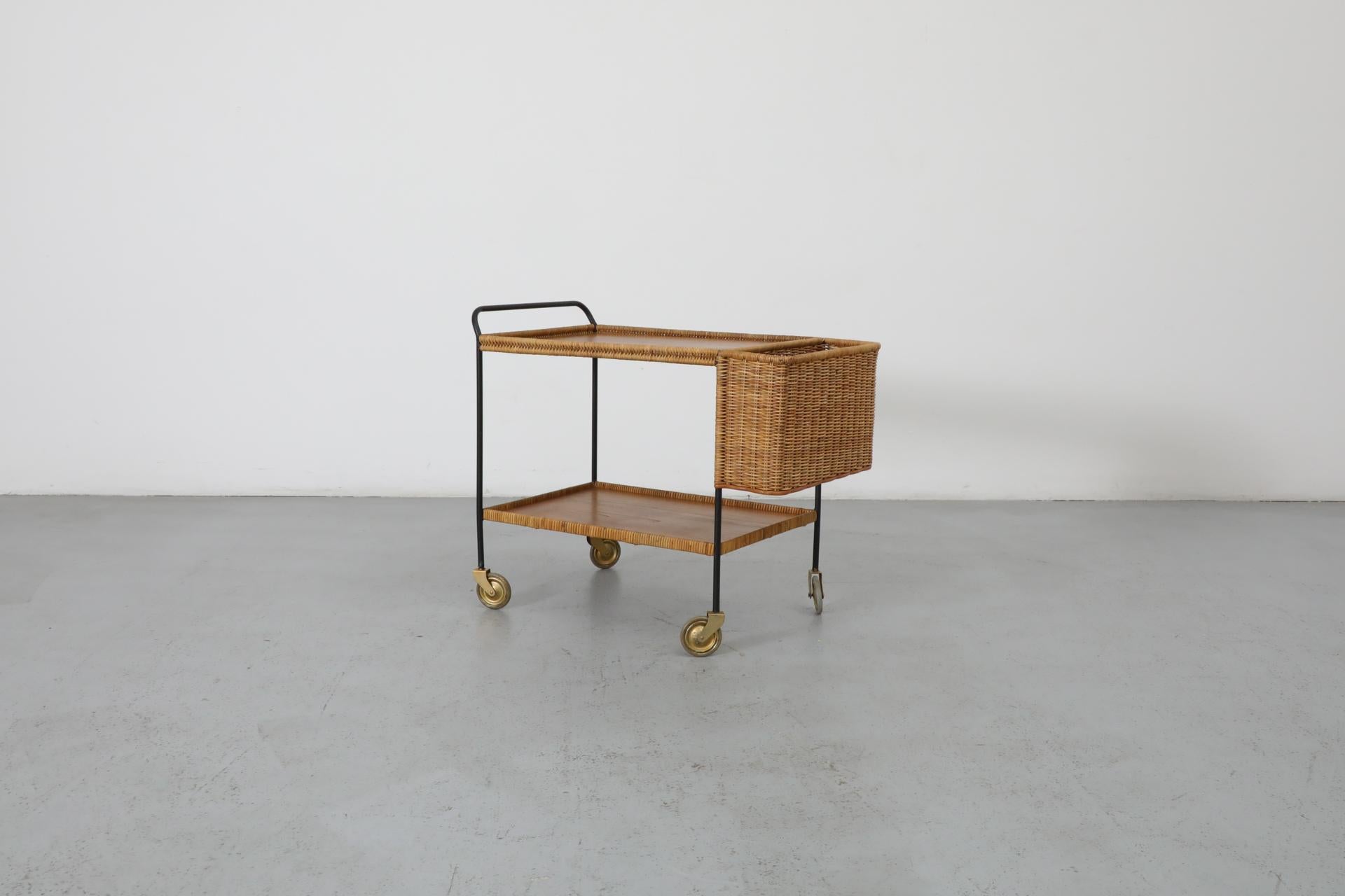 Chariot de bar en métal émaillé noir conçu par Helmut Magg pour Deutsche Werkstätten GmbH, Allemagne, années 1960. Équipé d'un compartiment à bouteilles en rotin, de deux niveaux de plateaux en placage de teck avec garniture en rotin et de roues en