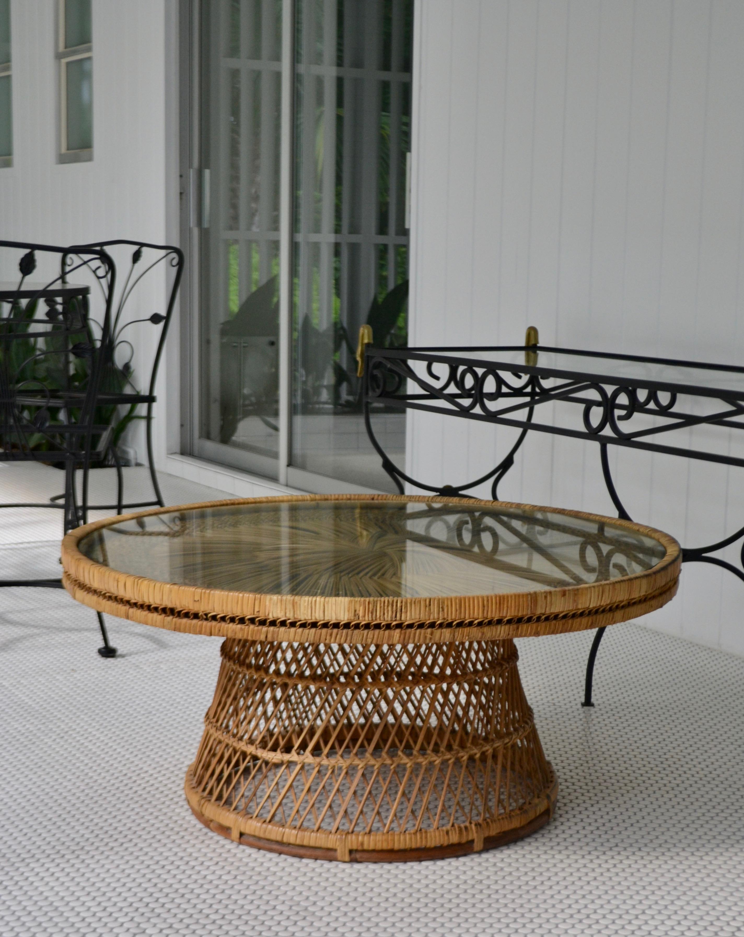 Stunning natural woven rattan round coffee table, circa 1960s. This striking midcentury cocktail table is designed of an intricately webbed woven rattan pattern over a wooden frame and outfitted with a round inset glass top.