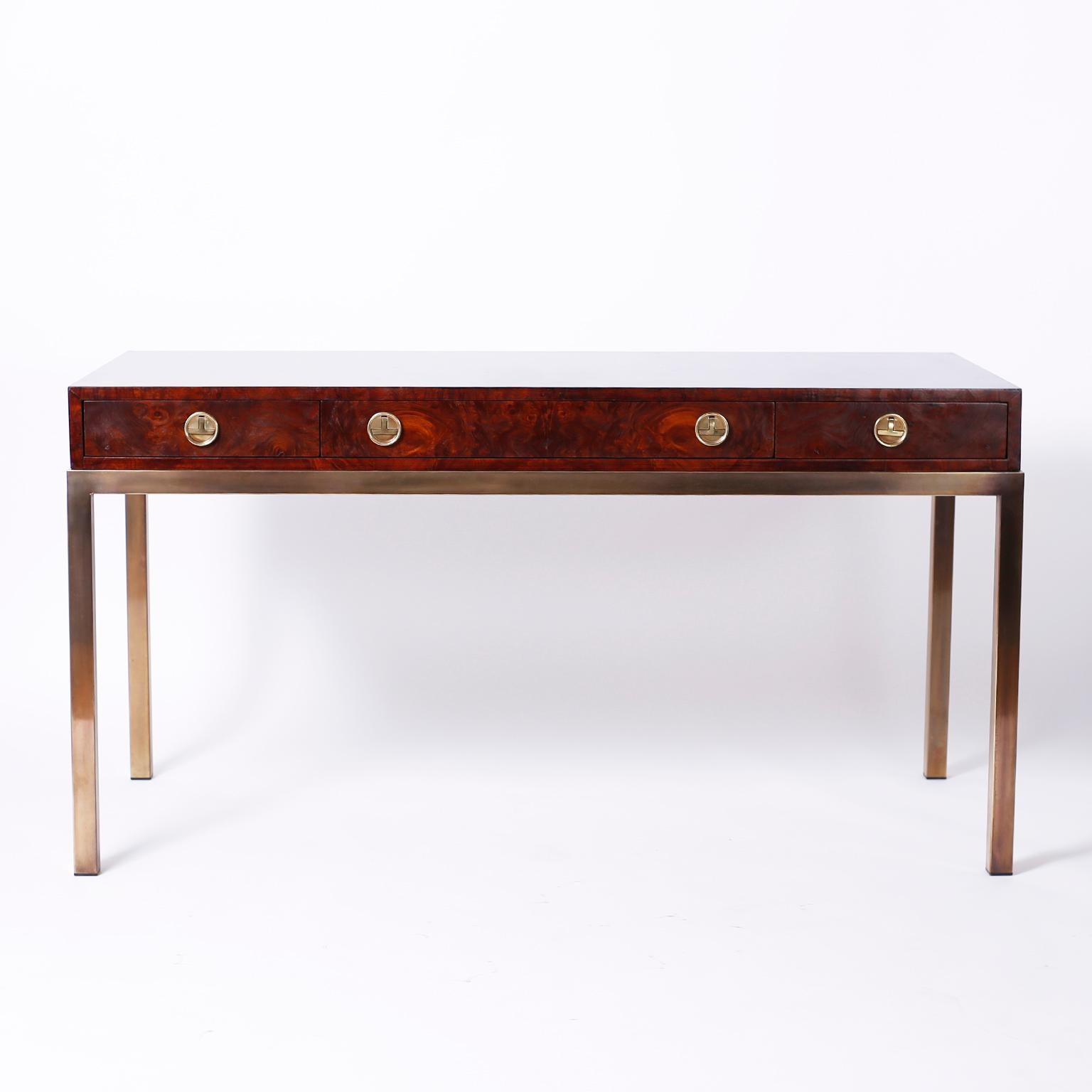 In vogue three-drawer writing desk with a lush custom finish over well grained burled walnut on all four sides, stylized brass Campaign hardware and elegant lacquered brass legs. Signed Mastercraft in a drawer.
