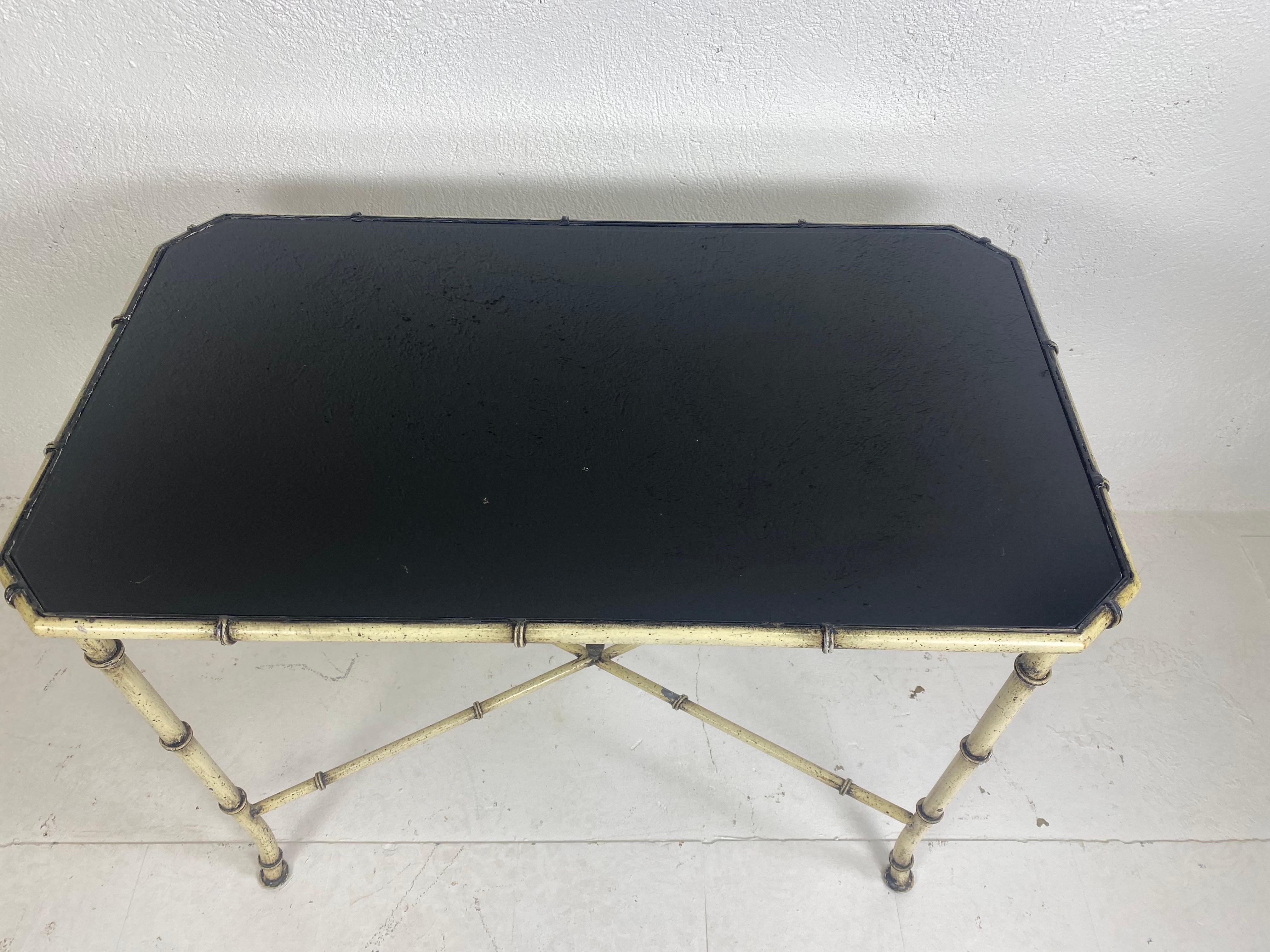 This is a mid-century vintage wrought iron and a black glass faux bamboo side table. The side table has an antique black-and-white finished the surface of the metal with a shiny black glass top this table was American made circa 1960.