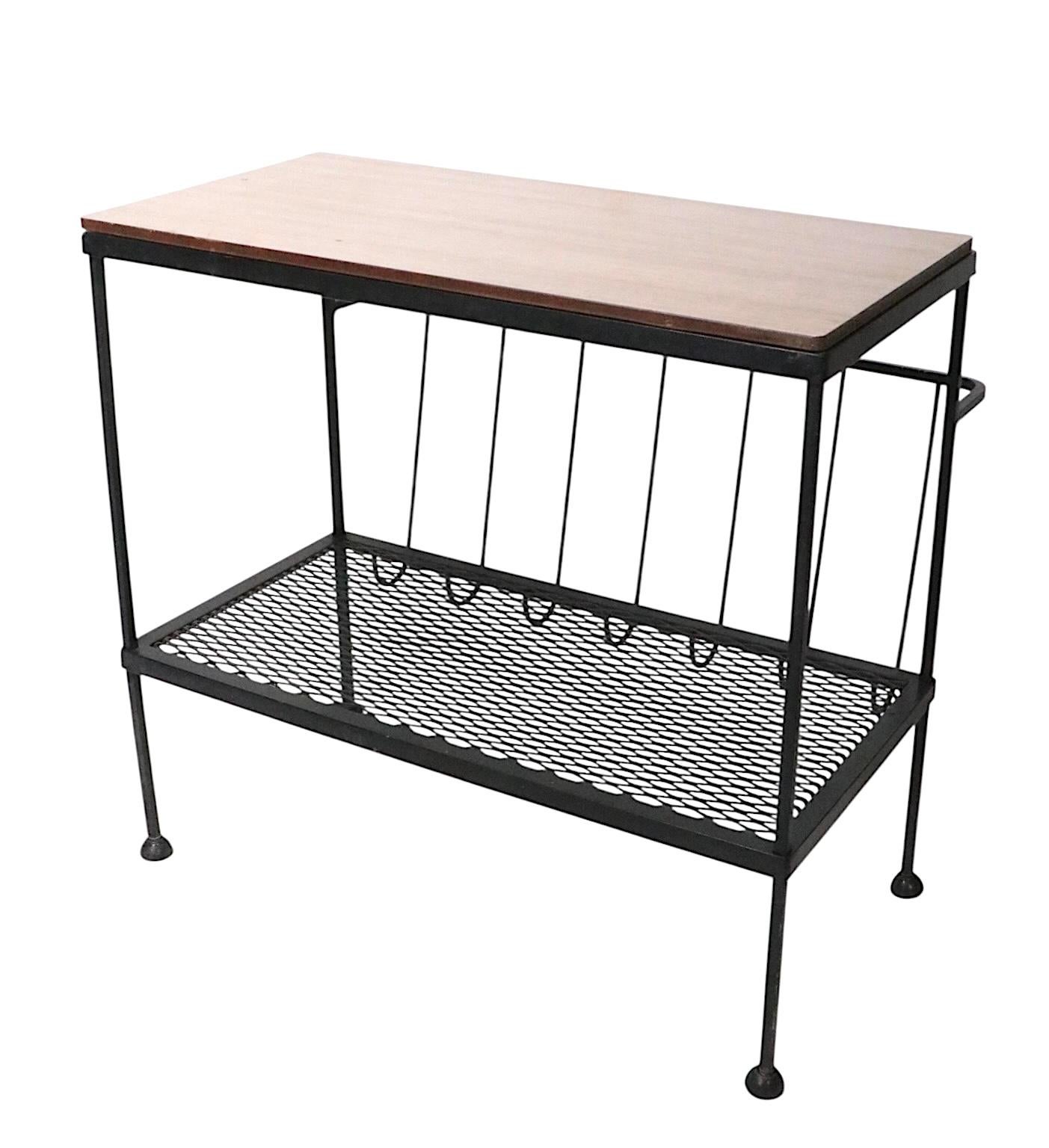 Architectural mid century end table, magazine rack made in the USA, by the Troy Sunshade Company 1950/60's. The stand features a faux wood grain formica top, supported by a wrought iron frame with a lower metal mesh shelf , and magazine rack. The