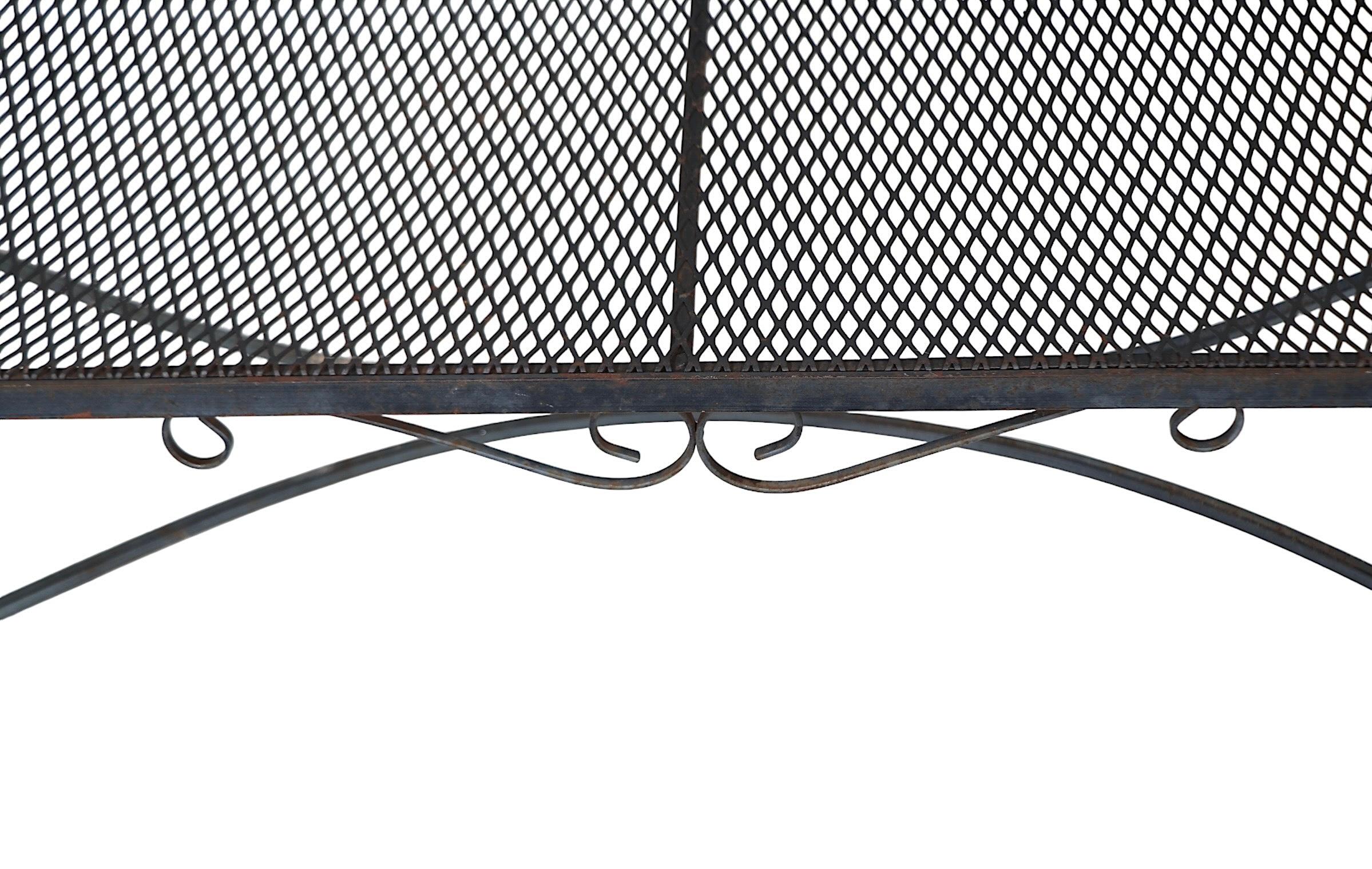 Jardin, patio, bord de piscine en fer forgé  canapé, causeuse par le  Woodard Furniture Company vers les années 1950/60. Ce canapé élégant est doté d'une structure décorative en fer forgé, d'un dossier et d'une assise en maille métallique. 
 Cet
